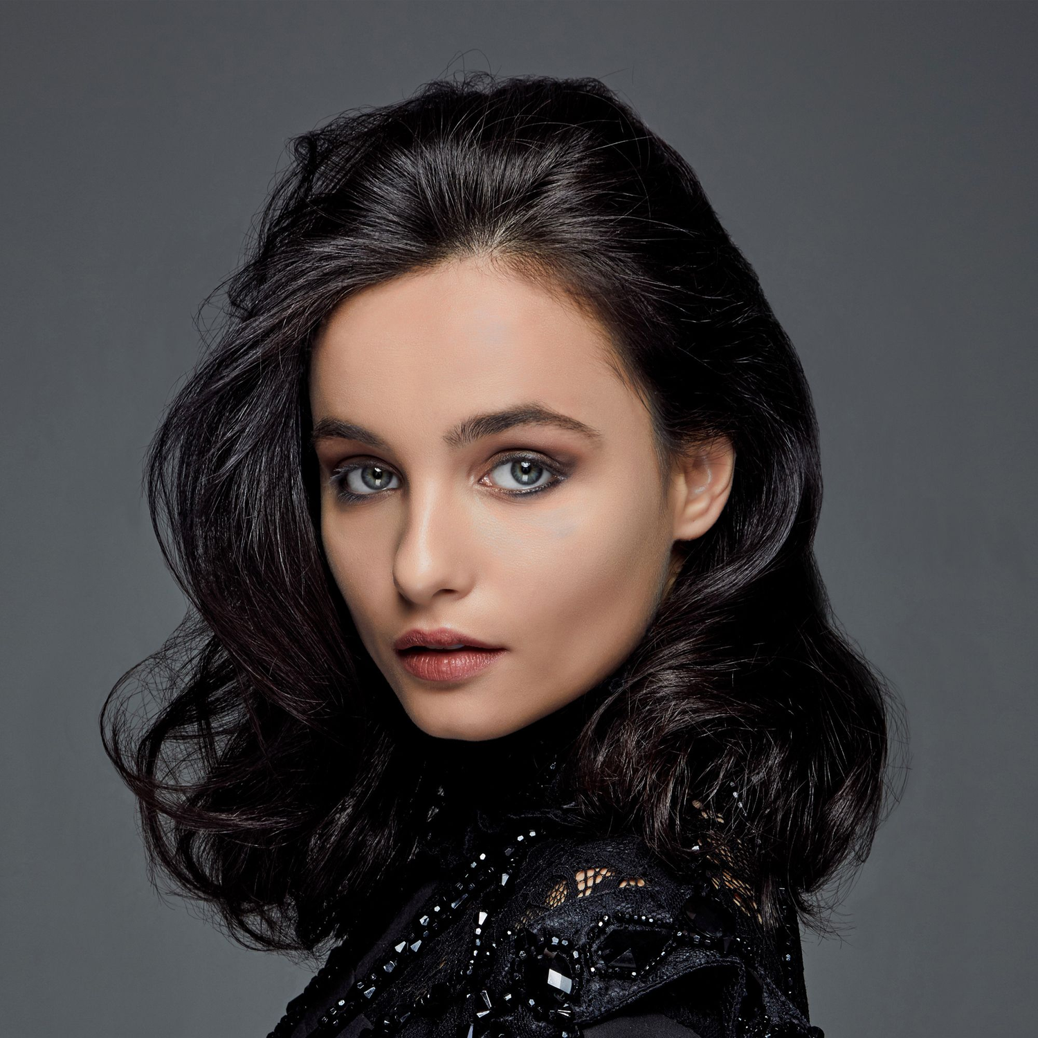 A portrait of a young woman with dark hair. She has gray eyes and is wearing a black top.