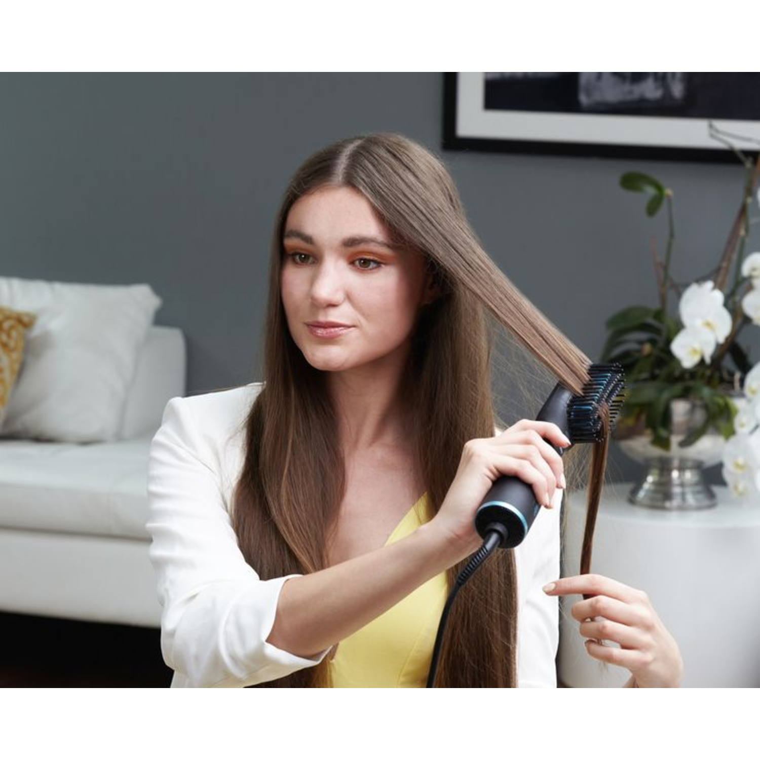 Vrouw die haar haar stylet met een zwart-blauwe haarborstel. Draagt een witte jas.