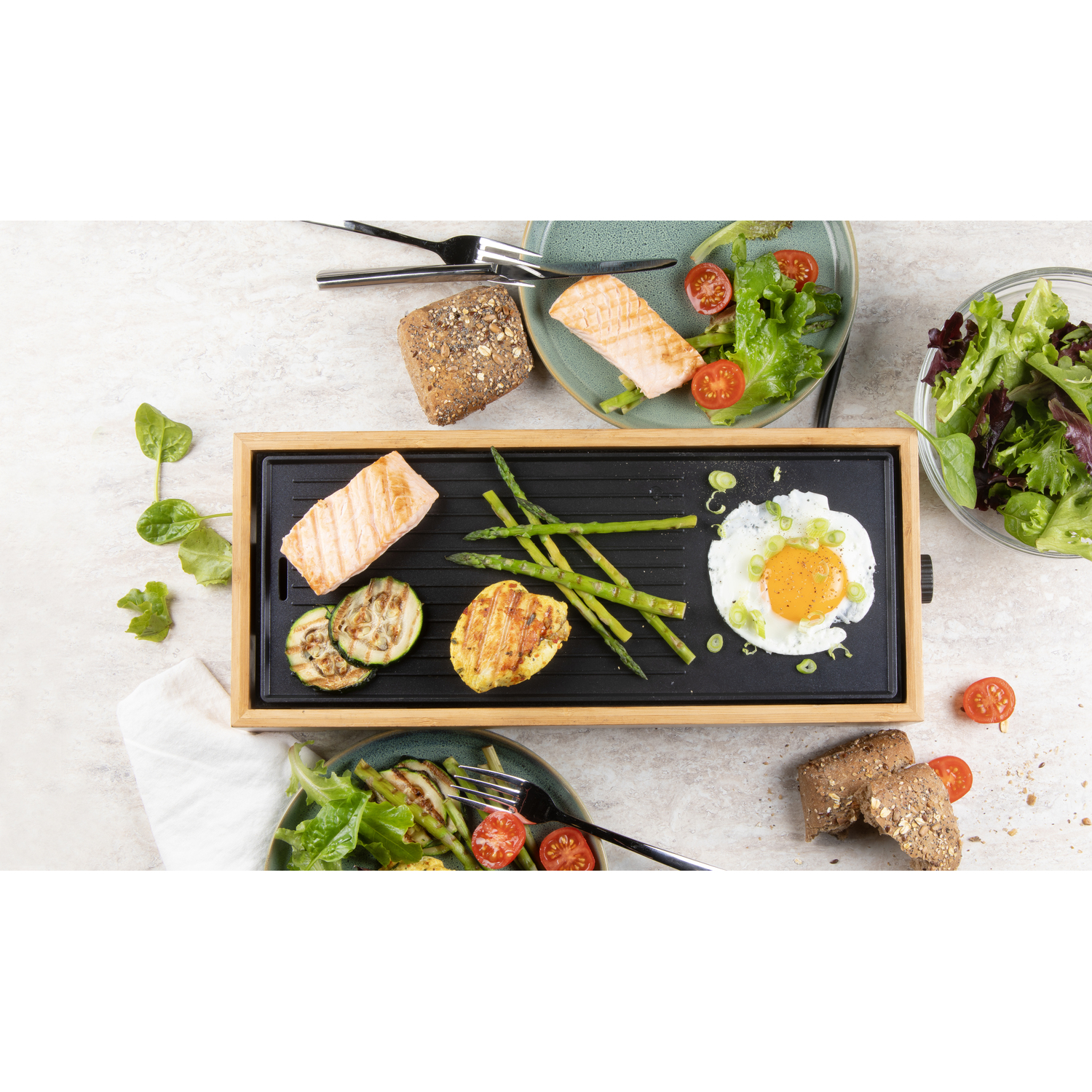 Plancha avec aliments cuits : saumon, légumes et œufs. Assiettes de salade.