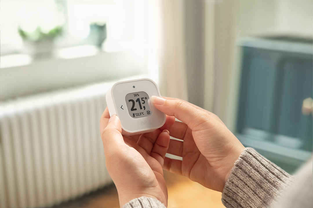 Egy személy kezei egy fehér okosotthon termosztátot tartanak.
