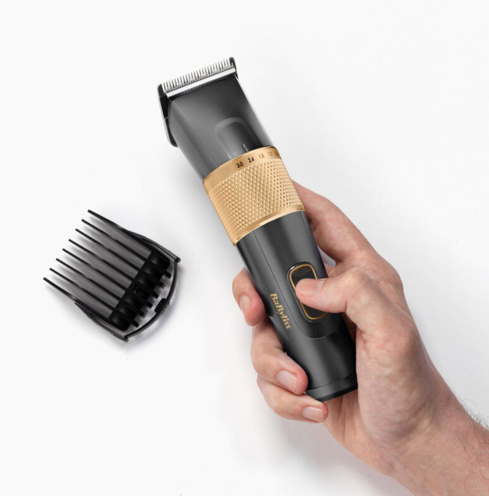Männerhand, die einen schwarzen und goldenen Haarschneider hält. Ein schwarzer Kunststoffkamm daneben.