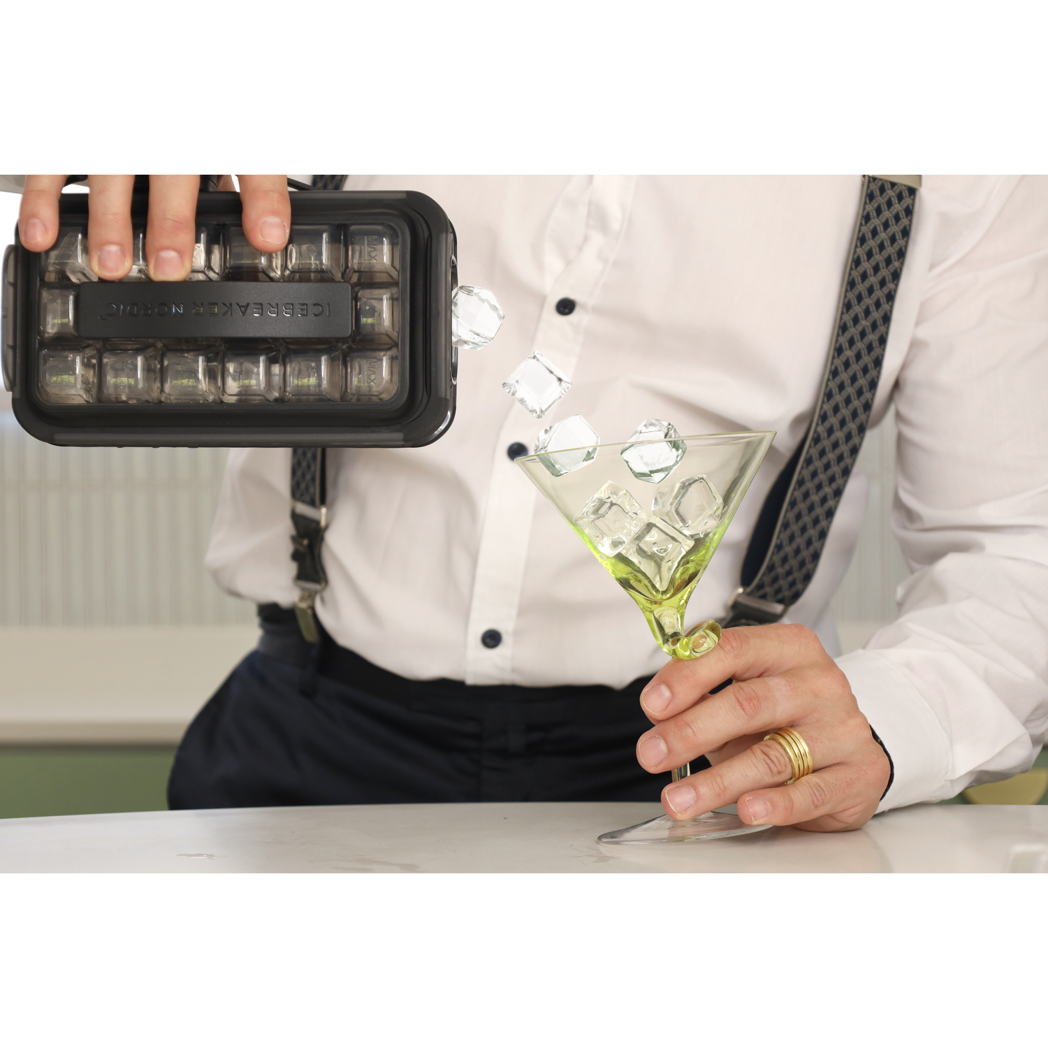 Een persoon giet ijsblokjes in een cocktailglas met een rietje.