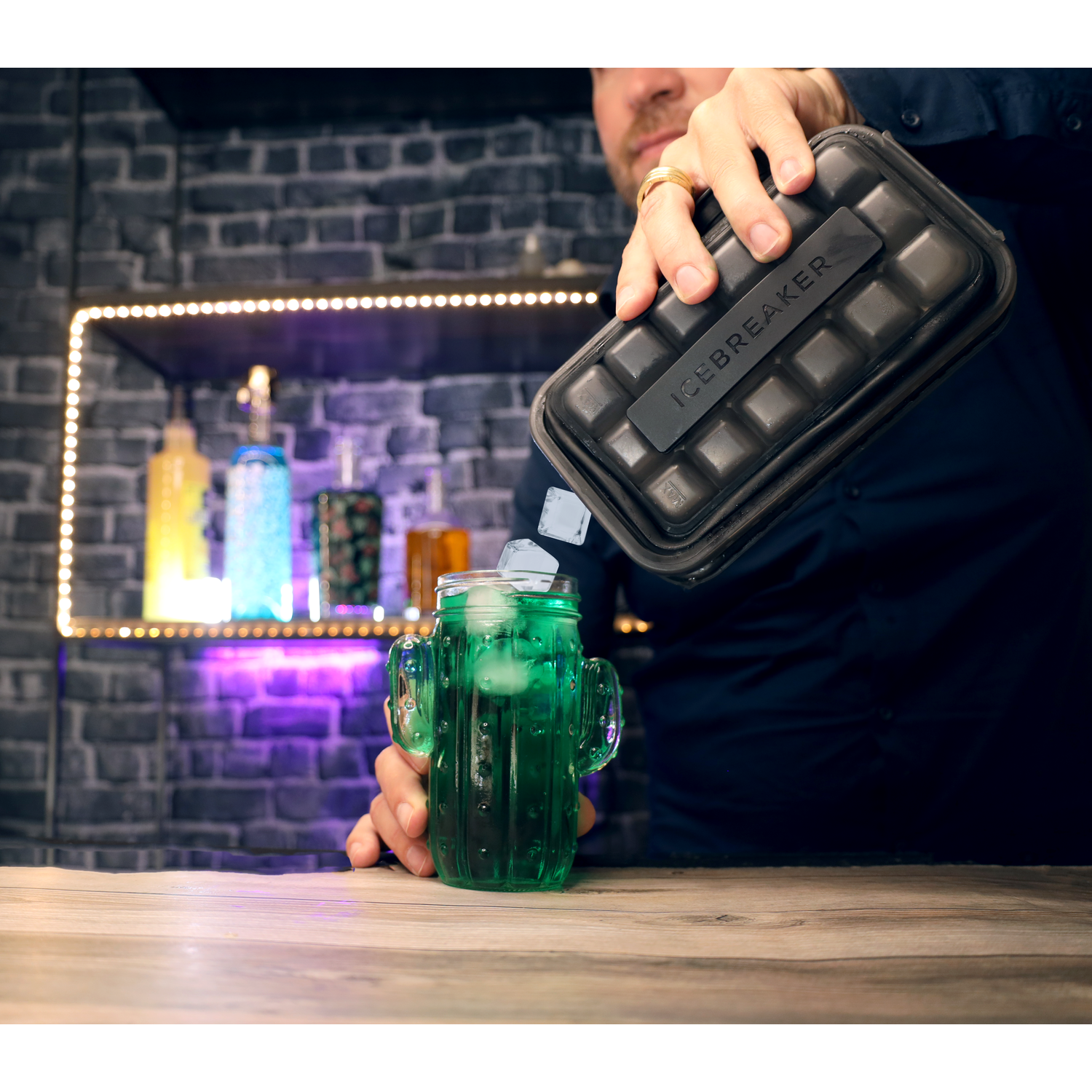 Man giet ijsblokjes uit een zwarte container in een groene cactusglas.