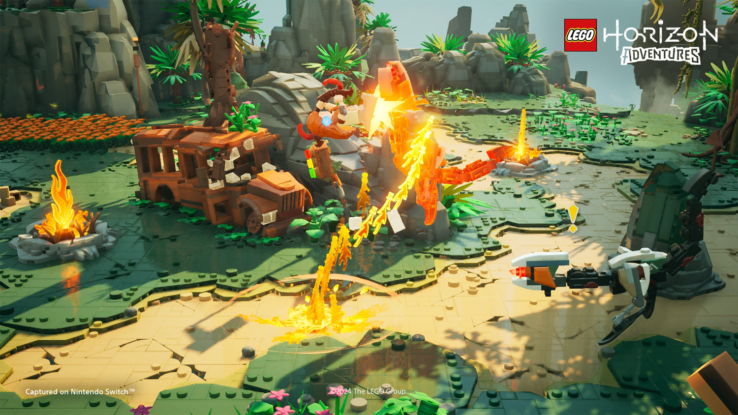Scena Lego Horizon Adventures con personaggi ed esplosioni su un ambiente sabbioso e verde.