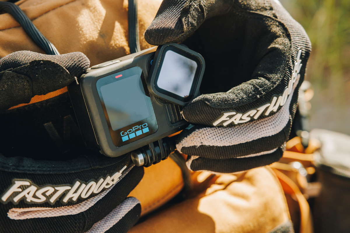 Hände halten eine GoPro, mit einem Filter und dem Text FASTHOUSE, auf verschwommenem Hintergrund.
