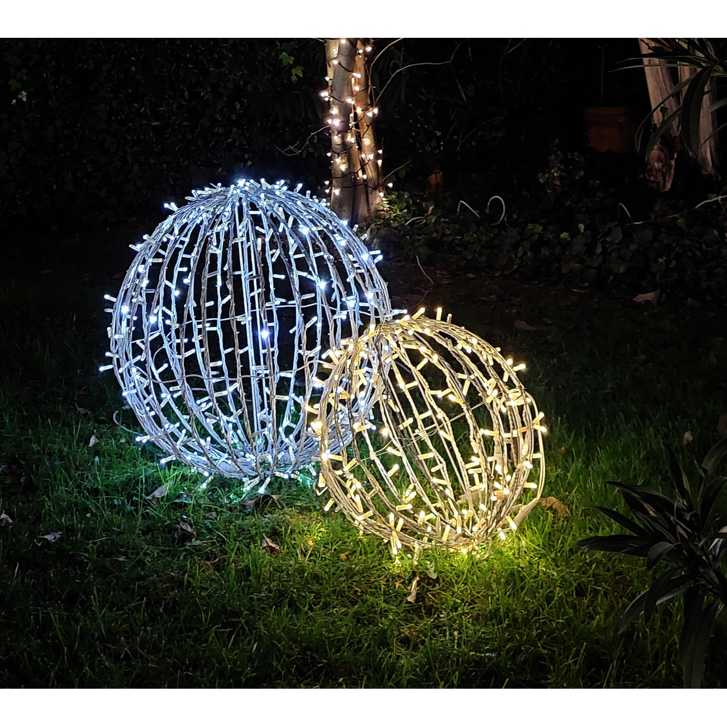 Due sfere illuminate, una bianca e una dorata, sull'erba di notte.