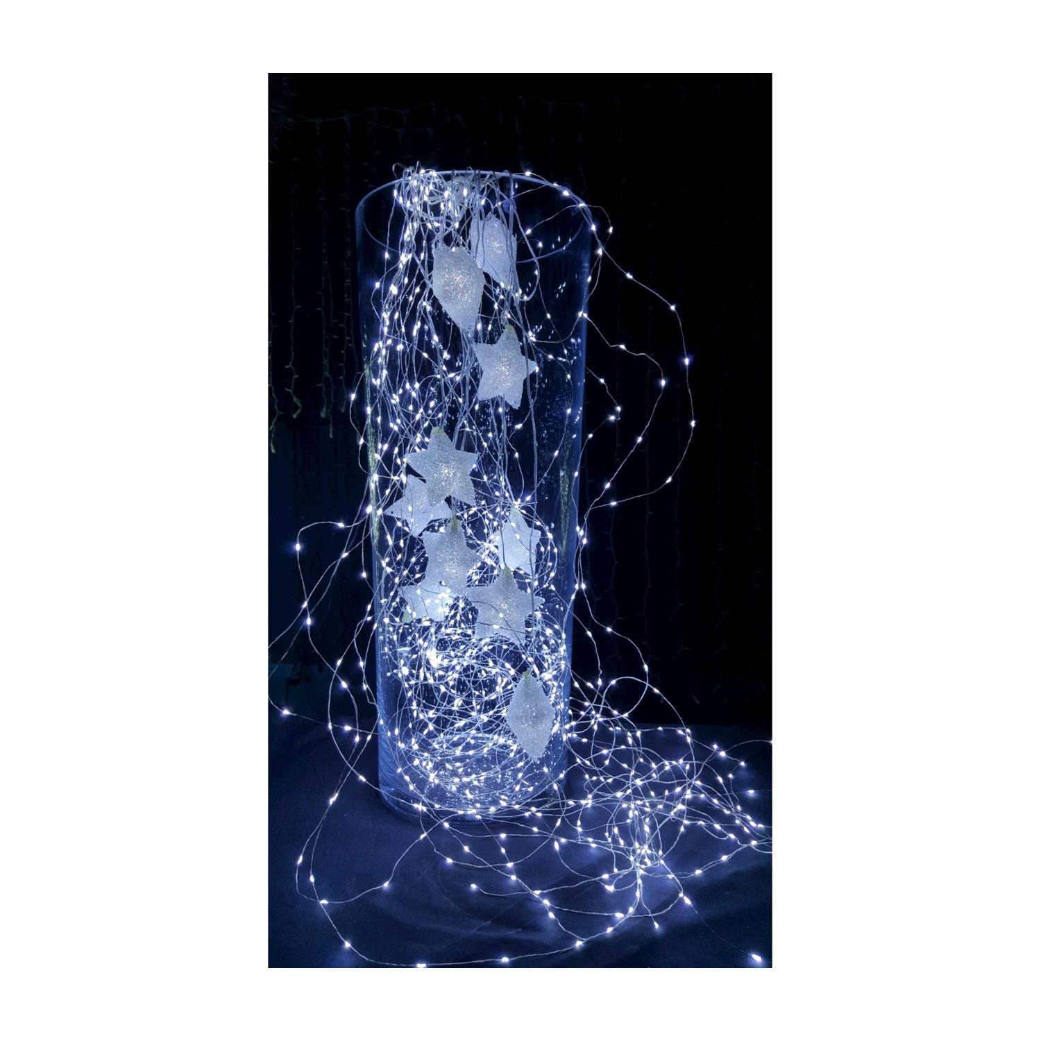Un vaso di vetro pieno di luci a filo bianche e decorazioni a forma di stella, sfondo scuro.