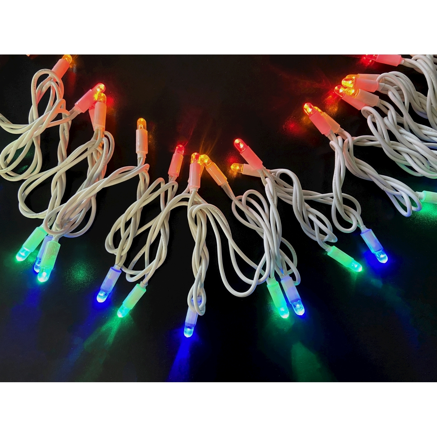 Luci di stringa con lampadine a LED multicolore su cablaggio bianco, su una superficie nera.