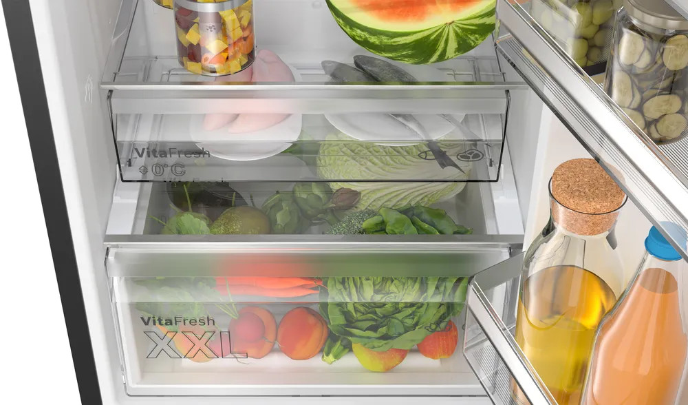 Otwarta lodówka z szufladami pełnymi jedzenia. W szufladach są warzywa i owoce.