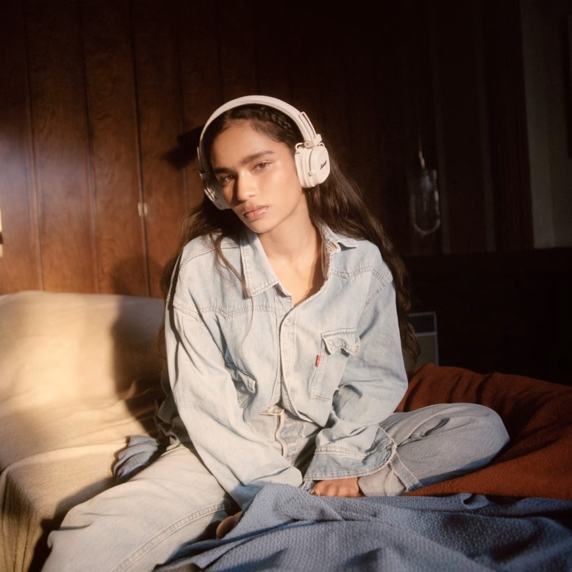 Donna con cuffie seduta su un letto con giacca di jeans e jeans.