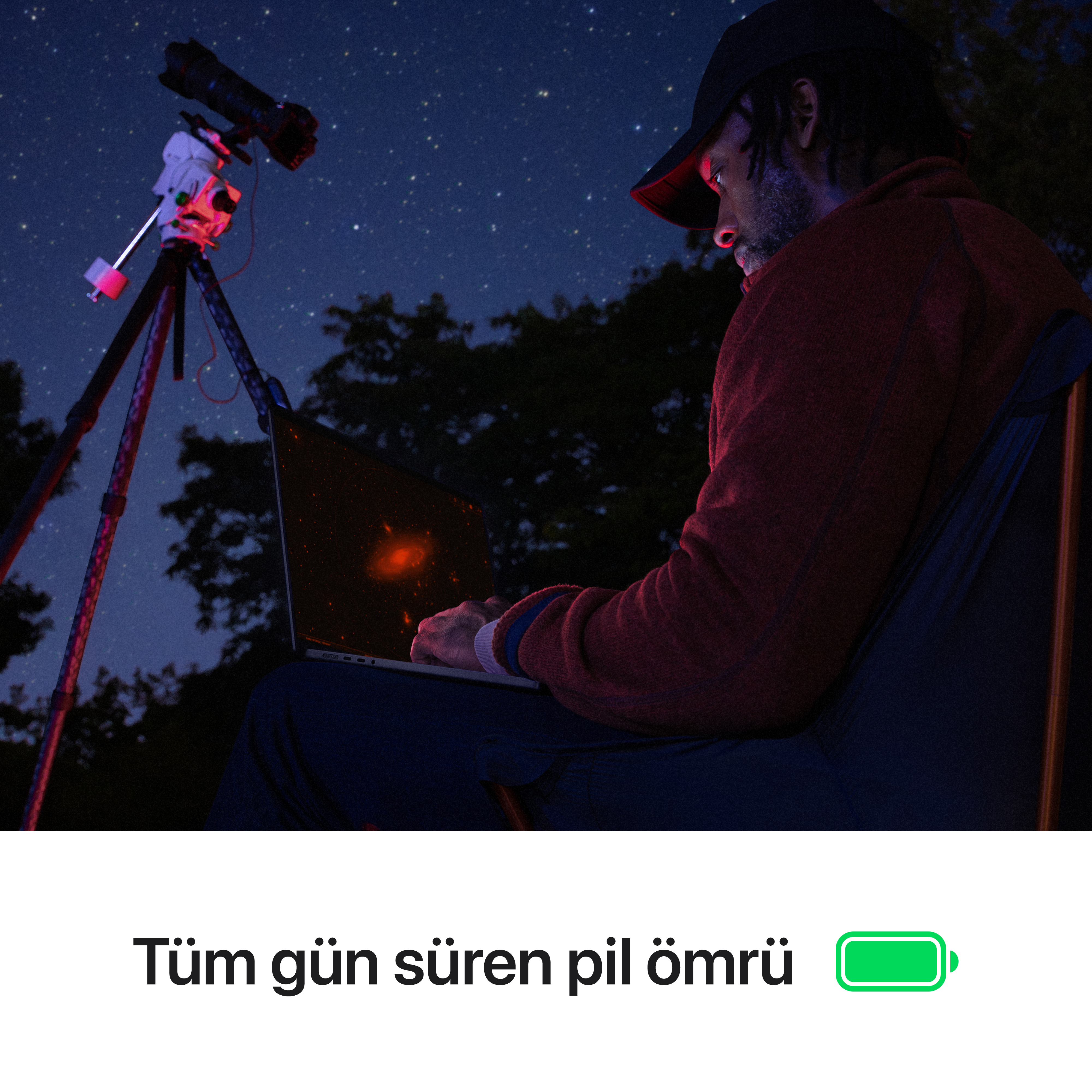 Adam gece laptop kullanıyor. Yakınlarda tripod üzerinde teleskop var. Karanlık gökyüzünü yıldızlar dolduruyor.