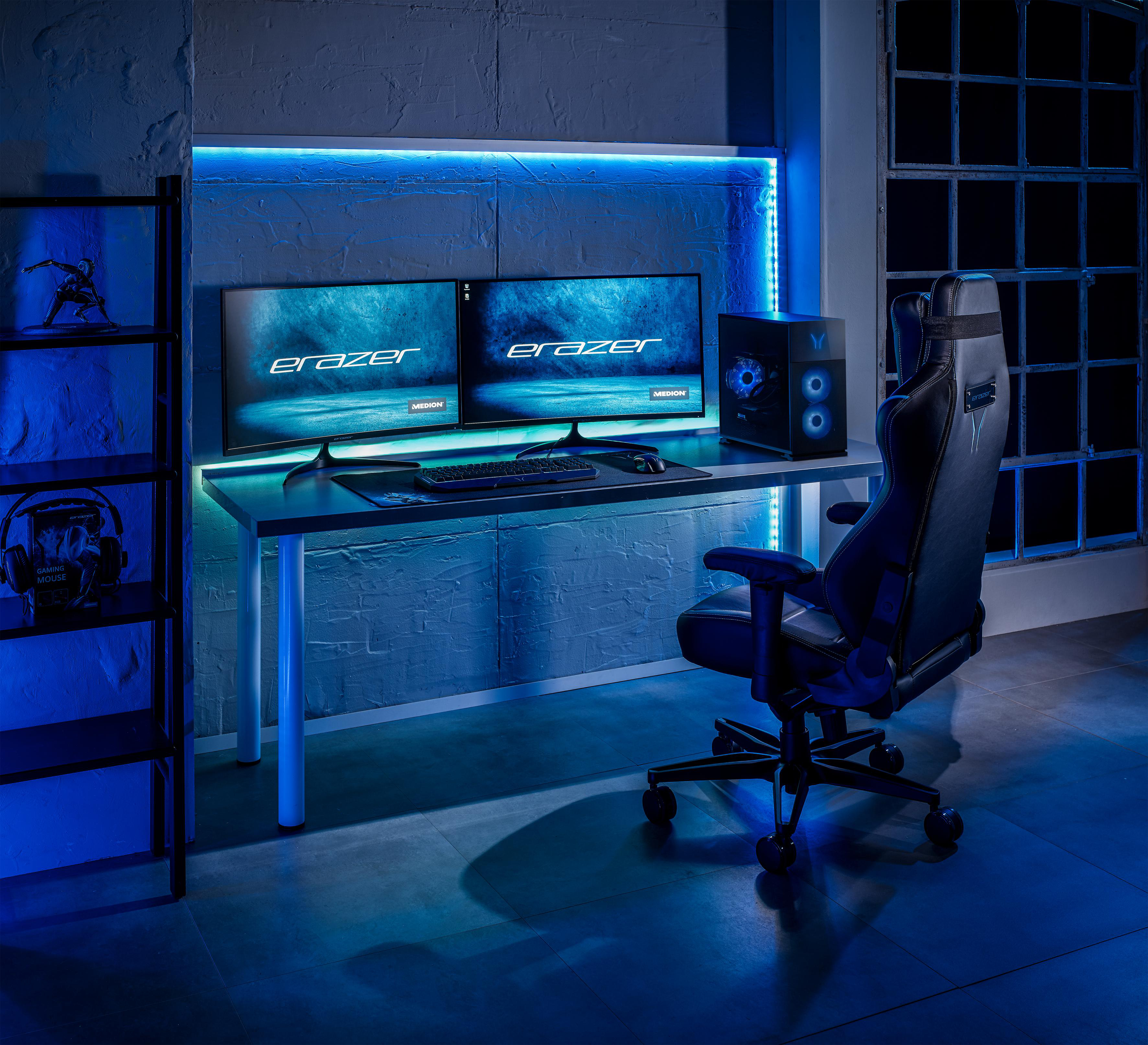 Gaming-Setup mit zwei Monitoren, Tastatur und Stuhl. Blaue Beleuchtung, schwarzer Hintergrund.