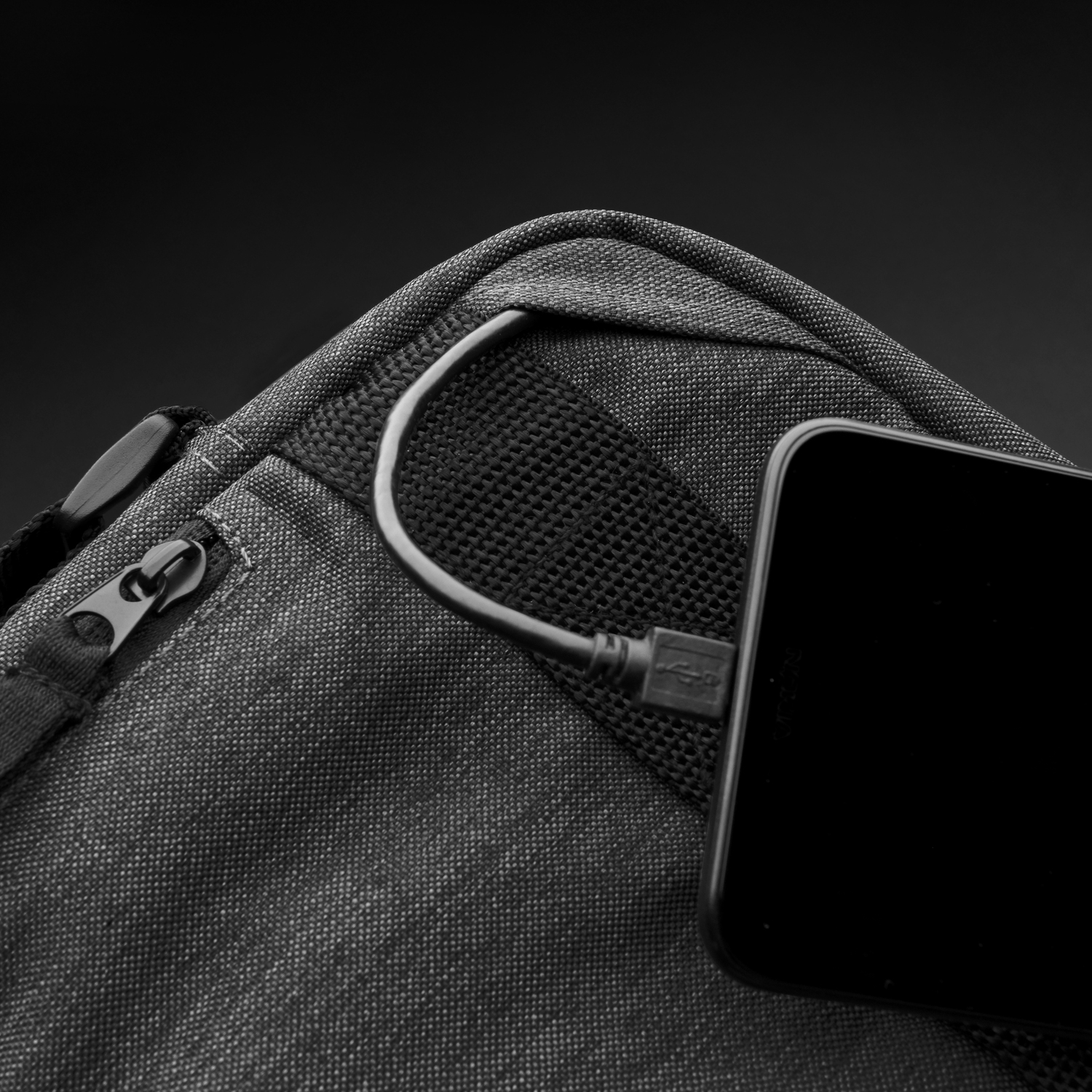 Close-up of a black bag with a zipper and a USB cable connected to a phone. Black background.