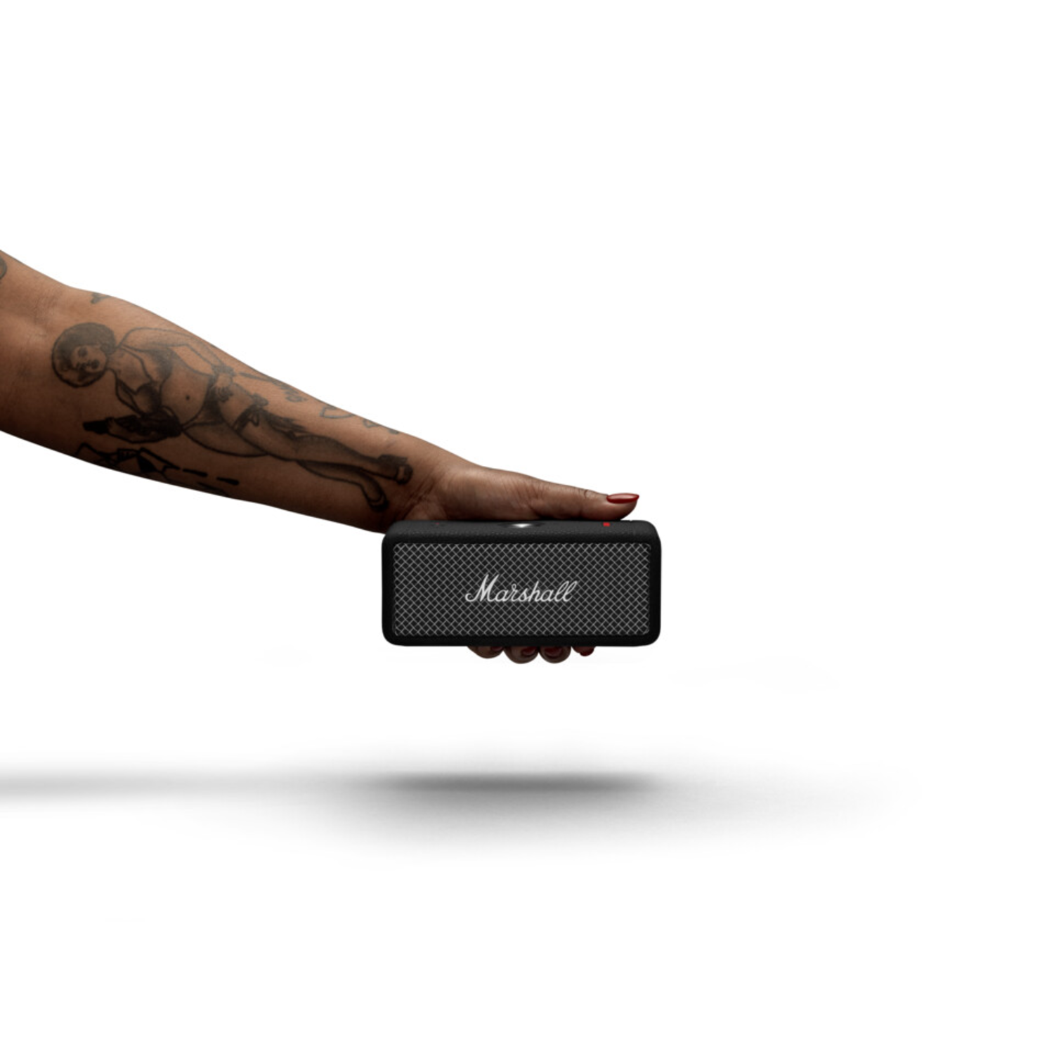 Hand holding a black Marshall speaker. Arm has a tattoo. White background.
