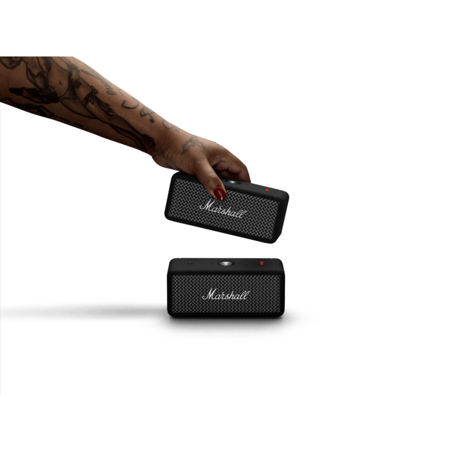 Hand holding Marshall speaker. Another speaker is below, both black.