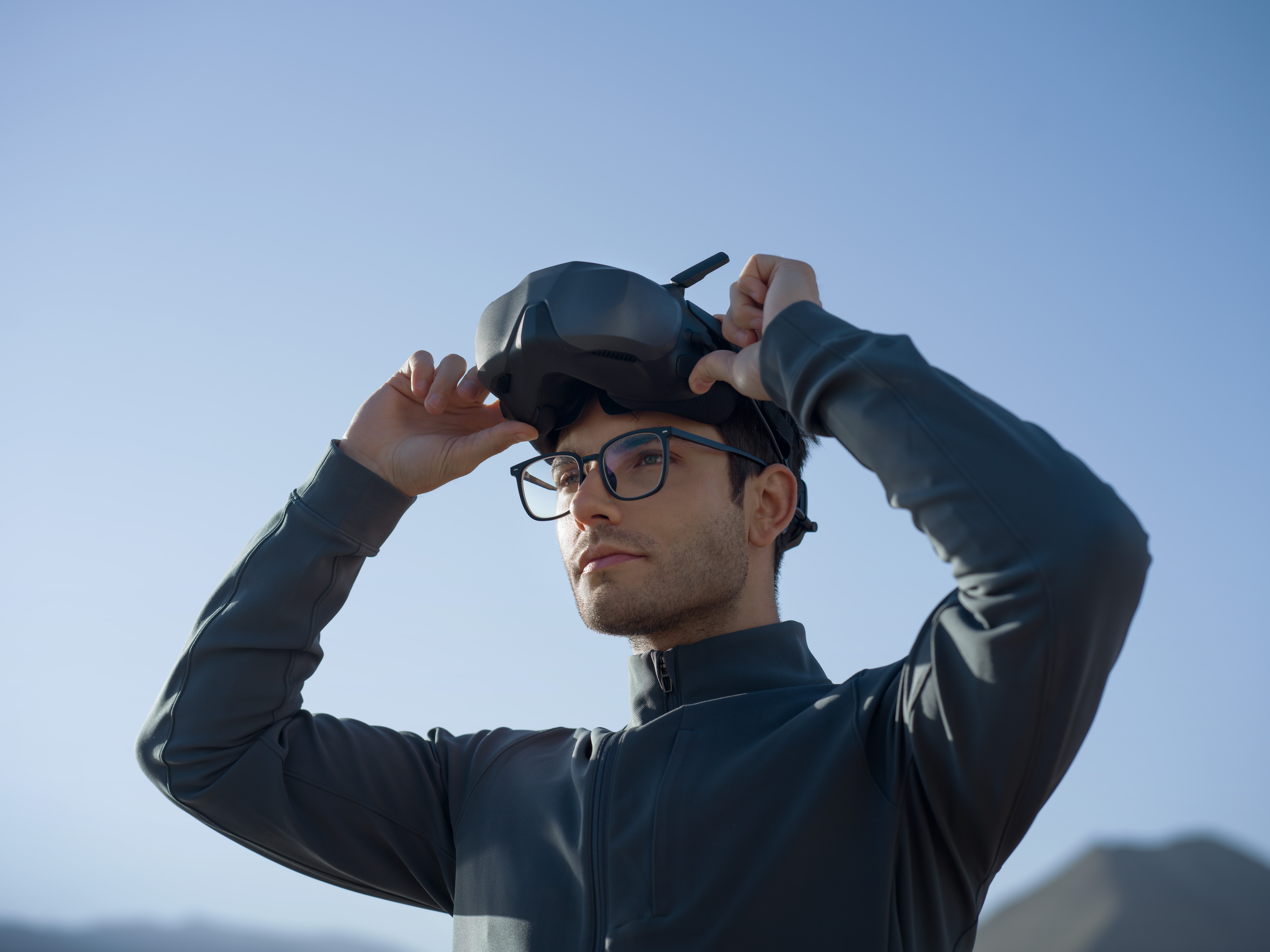 Ein Mann mit Brille setzt in einer sonnigen, äußeren Umgebung ein VR-Headset auf.