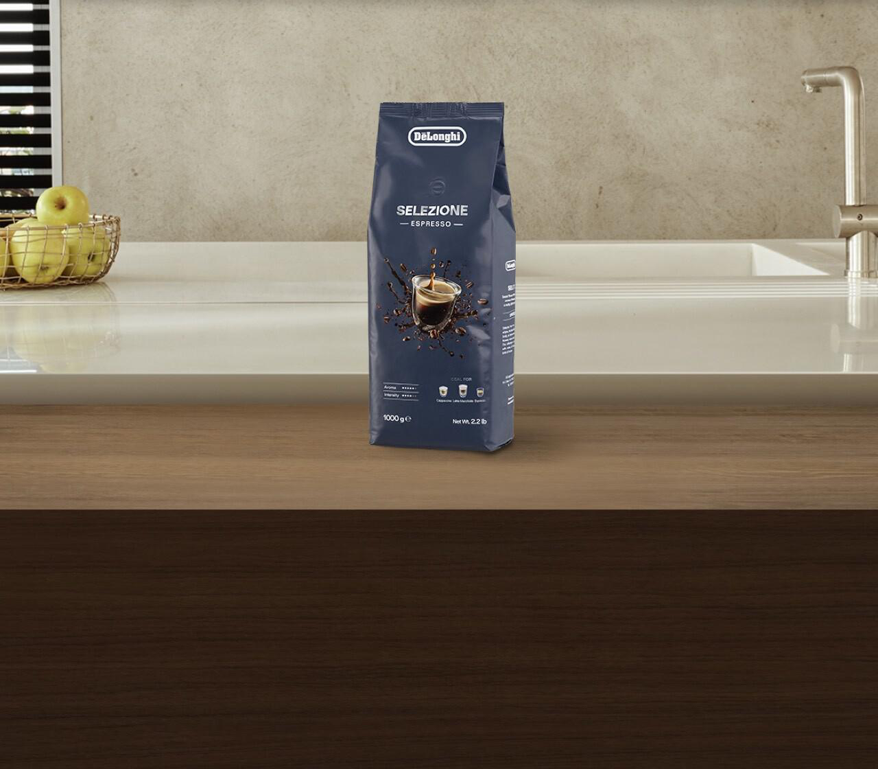 Eine Tüte Delonghi Selezione Espresso Kaffee auf einer Theke. Äpfel und ein Wasserhahn sind sichtbar.