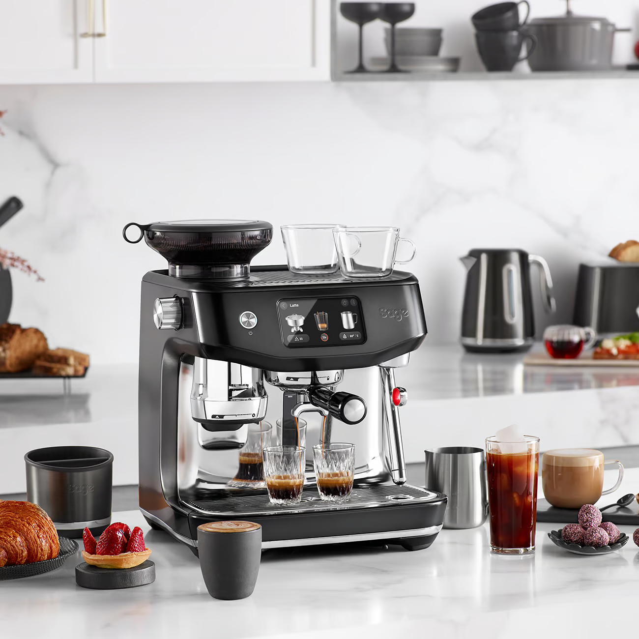 Una macchina per espresso nera, con varie preparazioni di caffè su un piano di lavoro bianco.