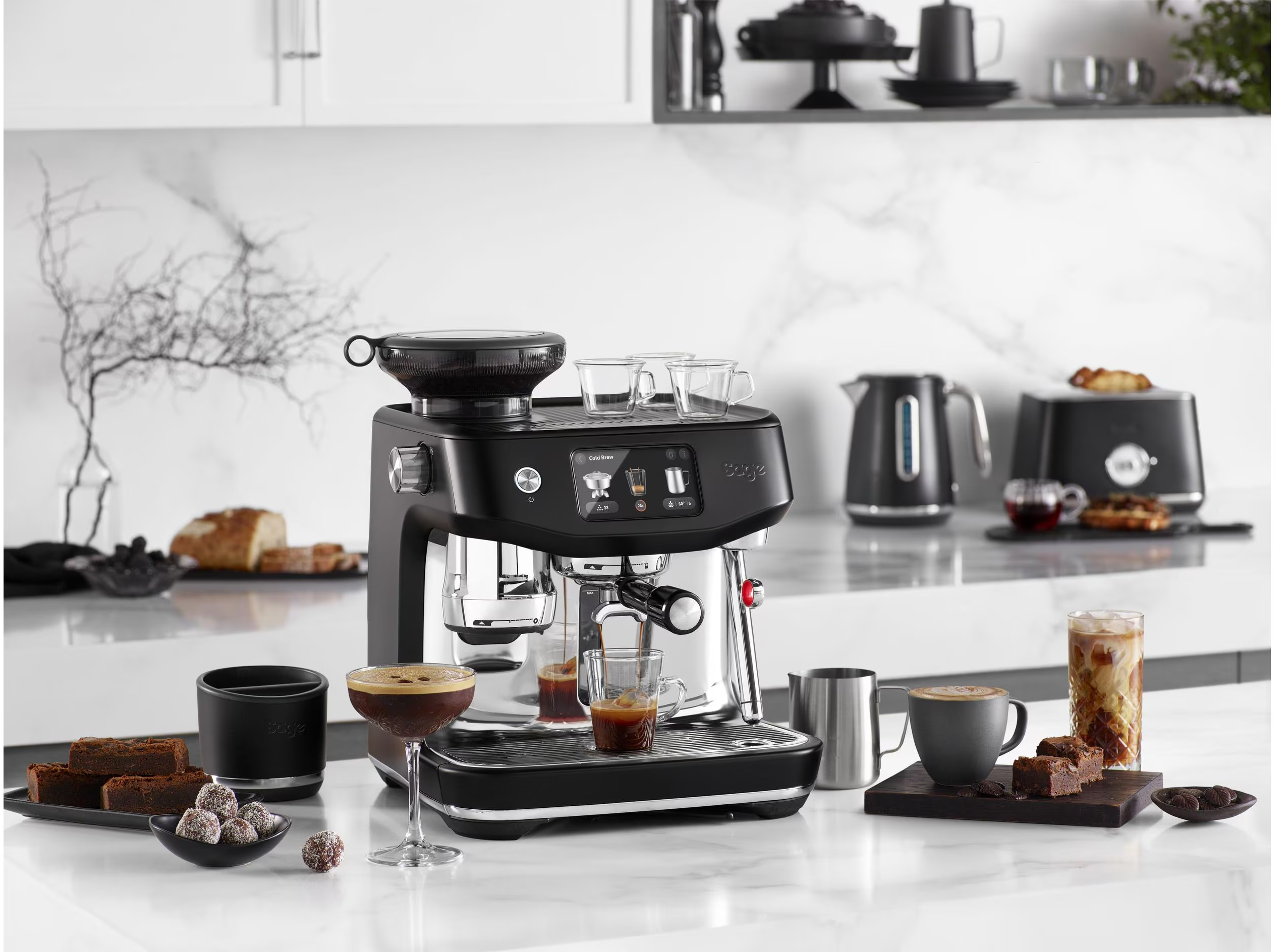 Macchina per espresso con varie bevande e pasticcini su un piano di lavoro in marmo bianco.