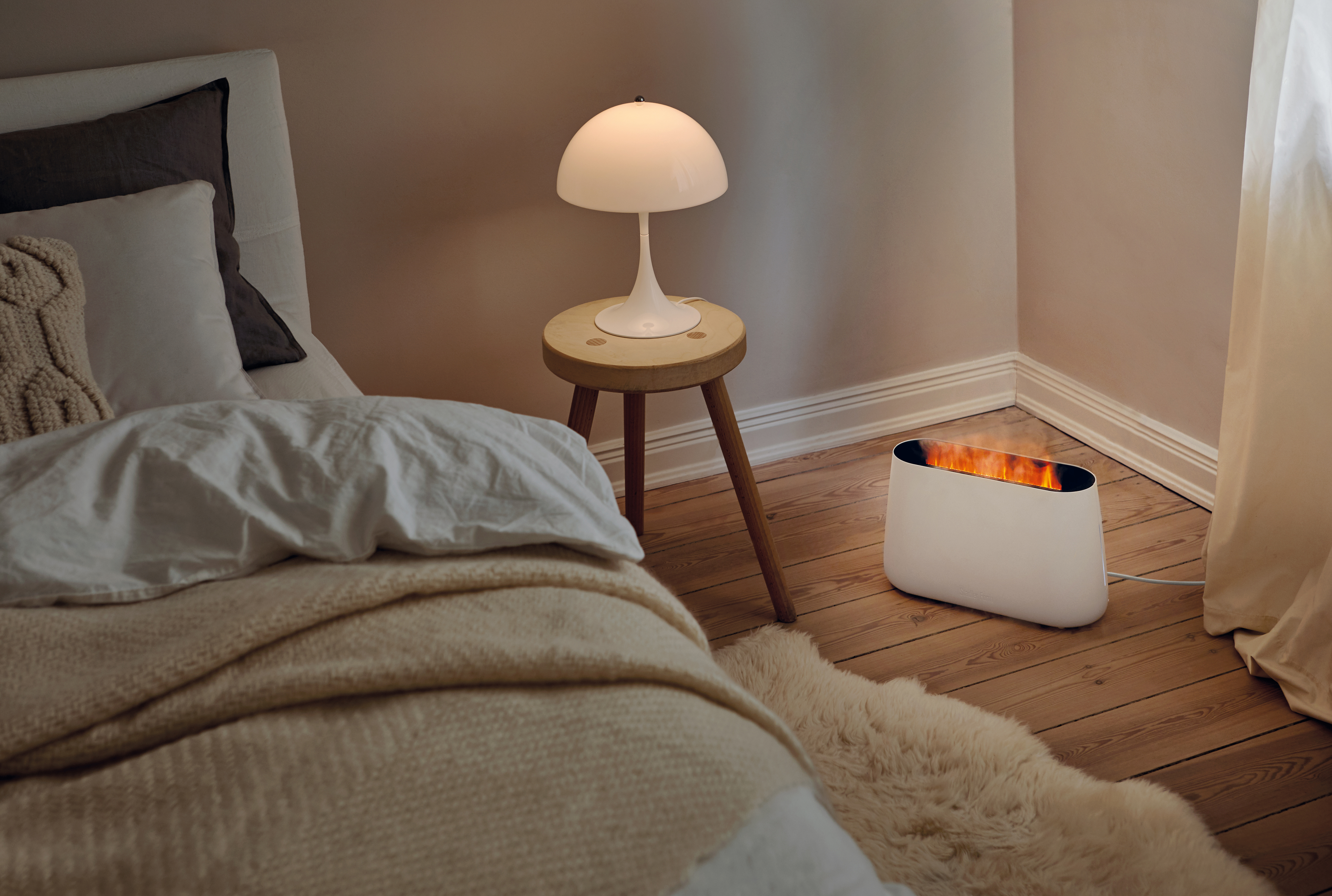 Zimmer mit einer weißen Lampe auf einem Hocker und einem weißen Heizkörper mit Flammeneffekt.