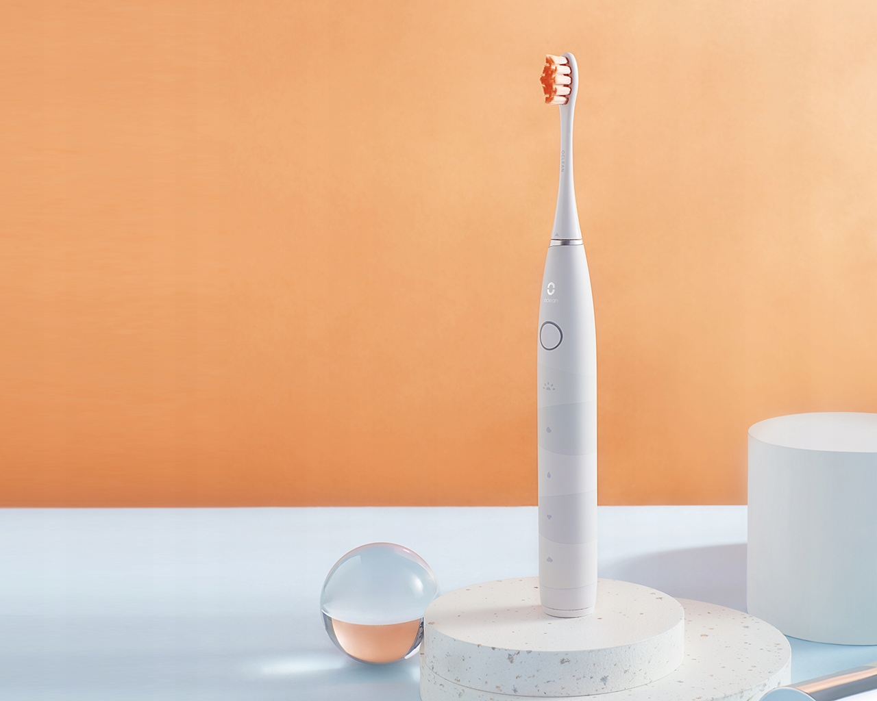 Szczoteczka elektryczna na stojaku. Biała z pomarańczowym włosiem i szklaną kulą.