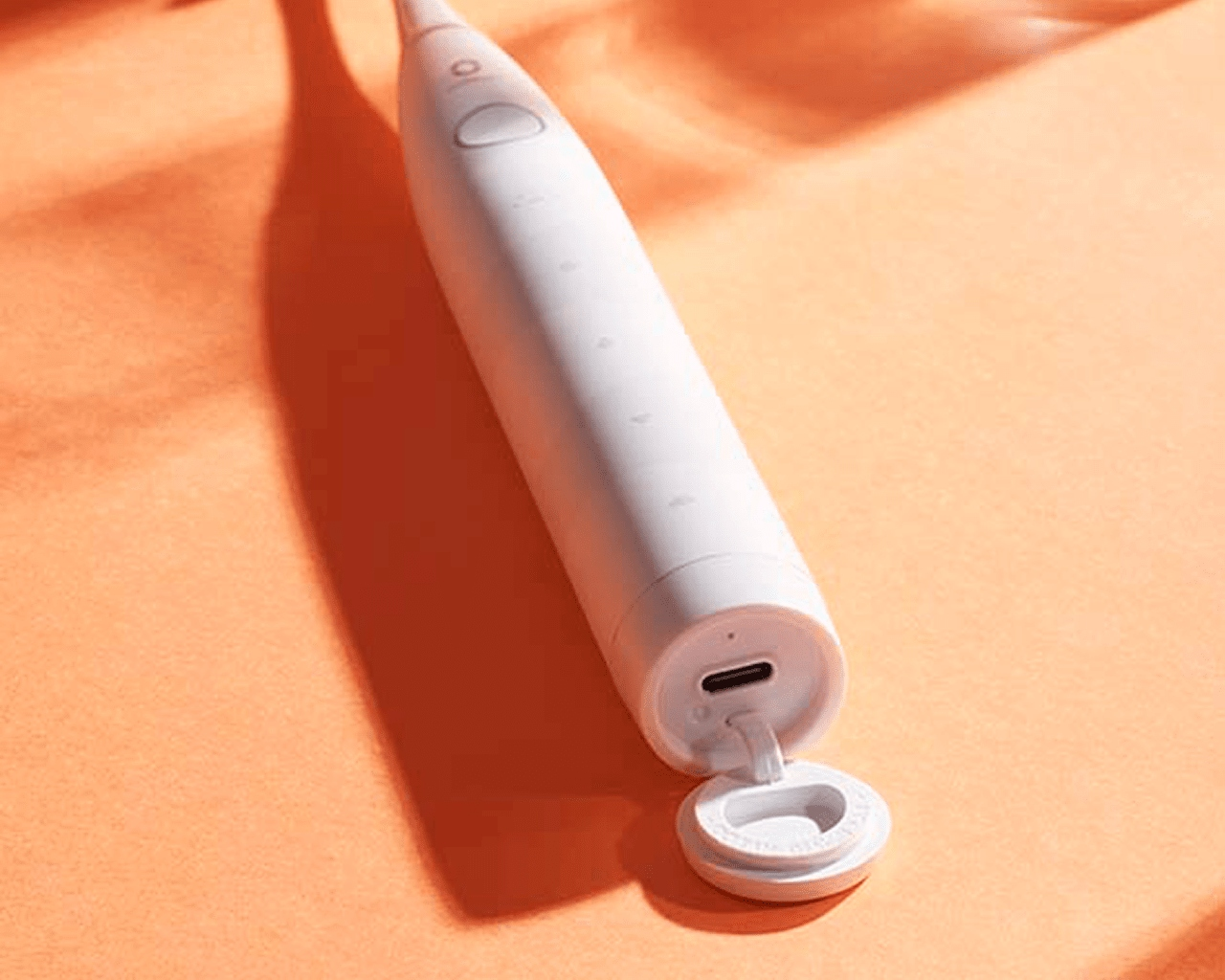 Biała szczoteczka elektryczna na pomarańczowym tle. Port USB jest otwarty.