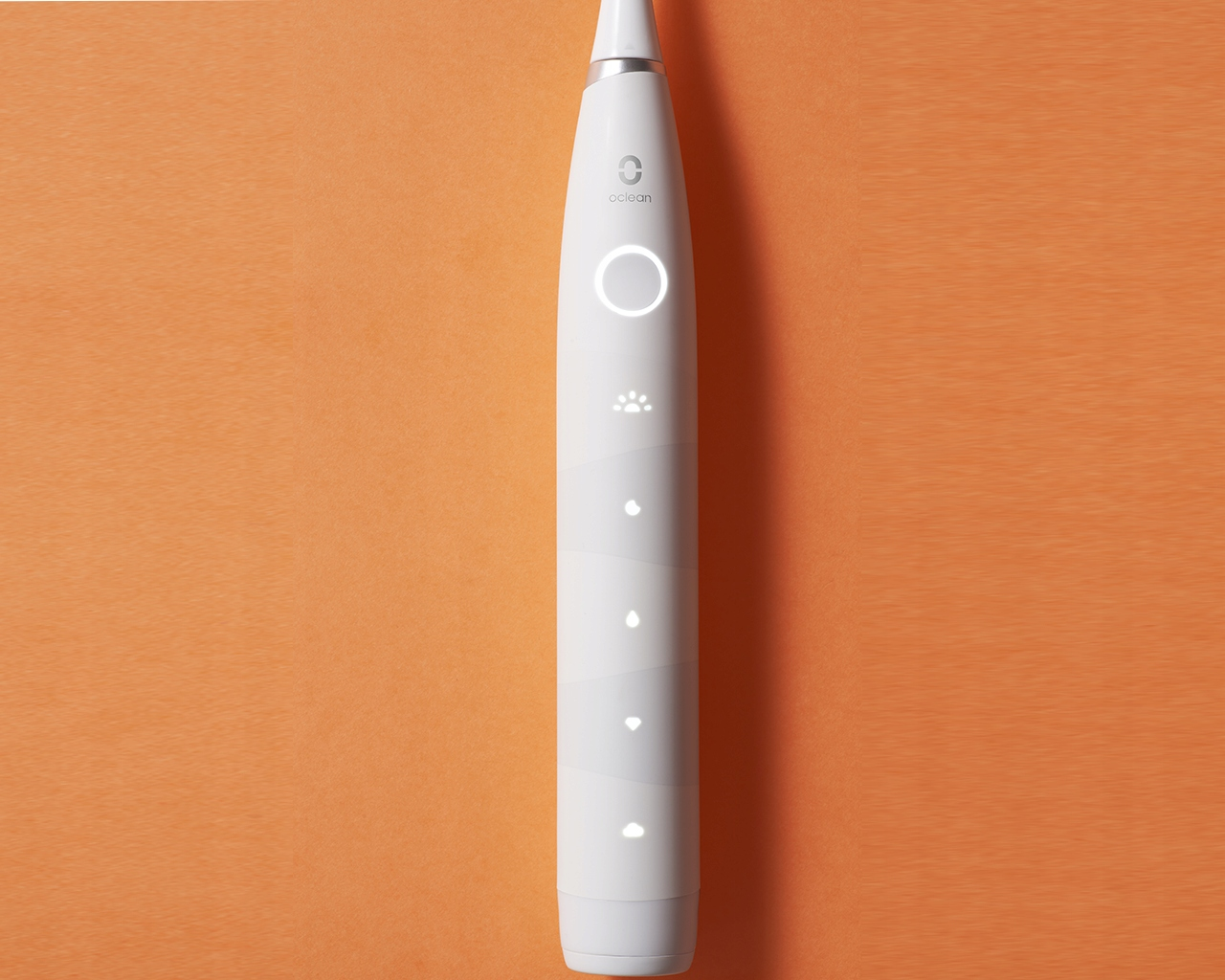 Biała elektryczna szczoteczka do zębów na pomarańczowym tle. Szczoteczka ma przycisk zasilania i inne lampki kontrolne.