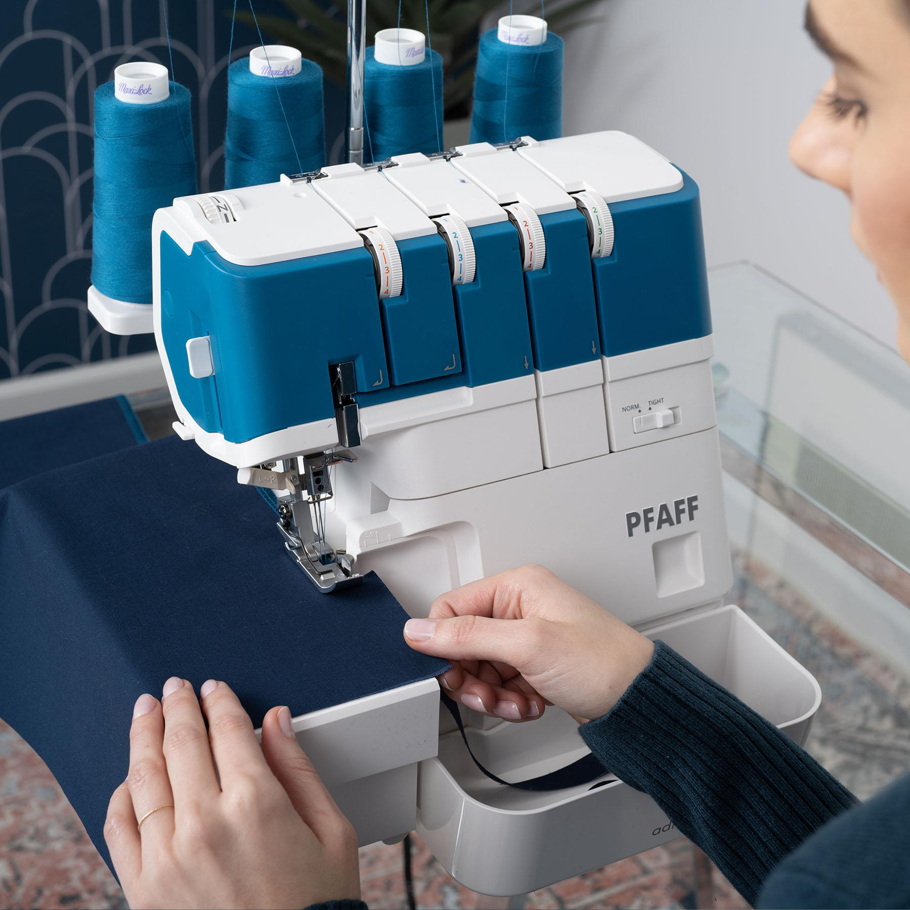 Eine Person benutzt eine blau-weiße Nähmaschine mit blauen Garnrollen im Hintergrund.