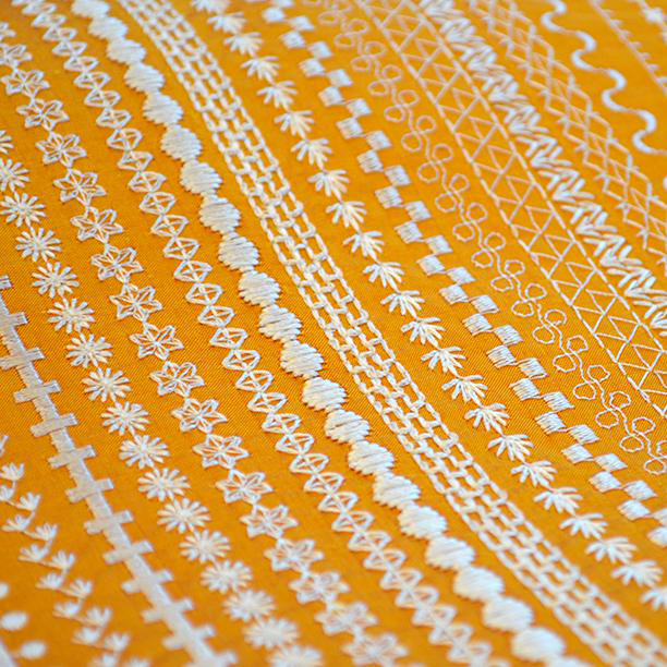 Gelber Stoff mit weißen Stickmustern. Verschiedene florale und geometrische Designs.