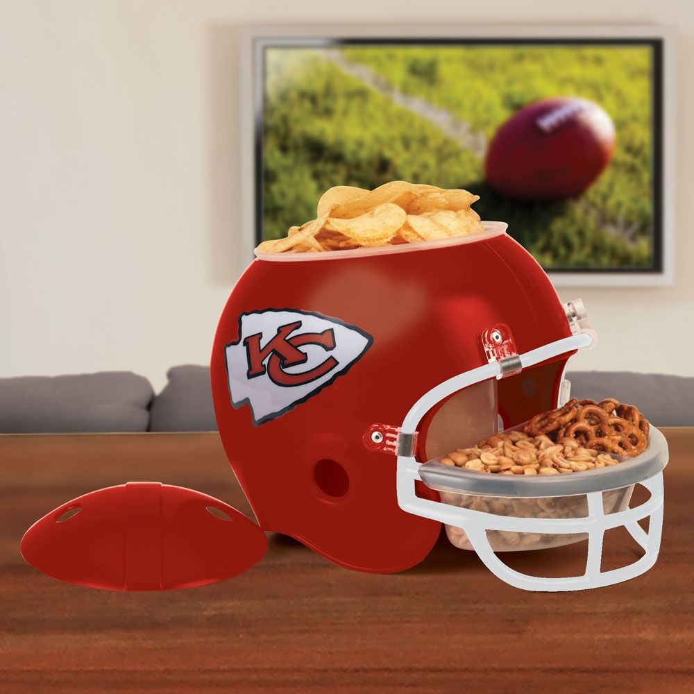 Ein roter Kansas City Chiefs Helm mit Chips und Snacks, ein Football im Hintergrund, auf einem Tisch.