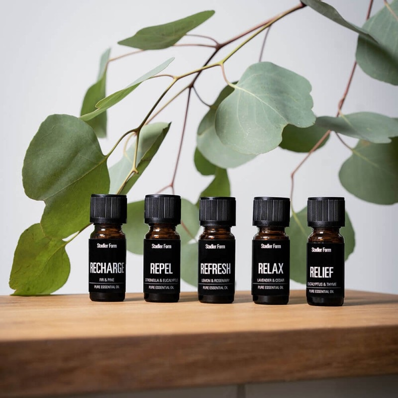 Pięć butelek olejku eterycznego na drewnianej powierzchni z zielenią.