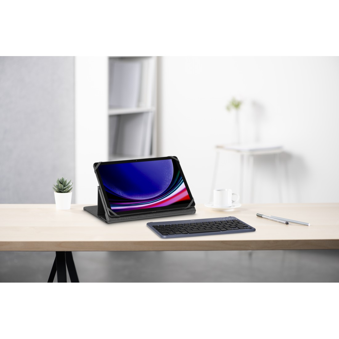 Tablet mit Tastatur auf Holzschreibtisch, kleine Pflanze, Stift und Kaffeetasse. Hintergrund: weiße Wand.