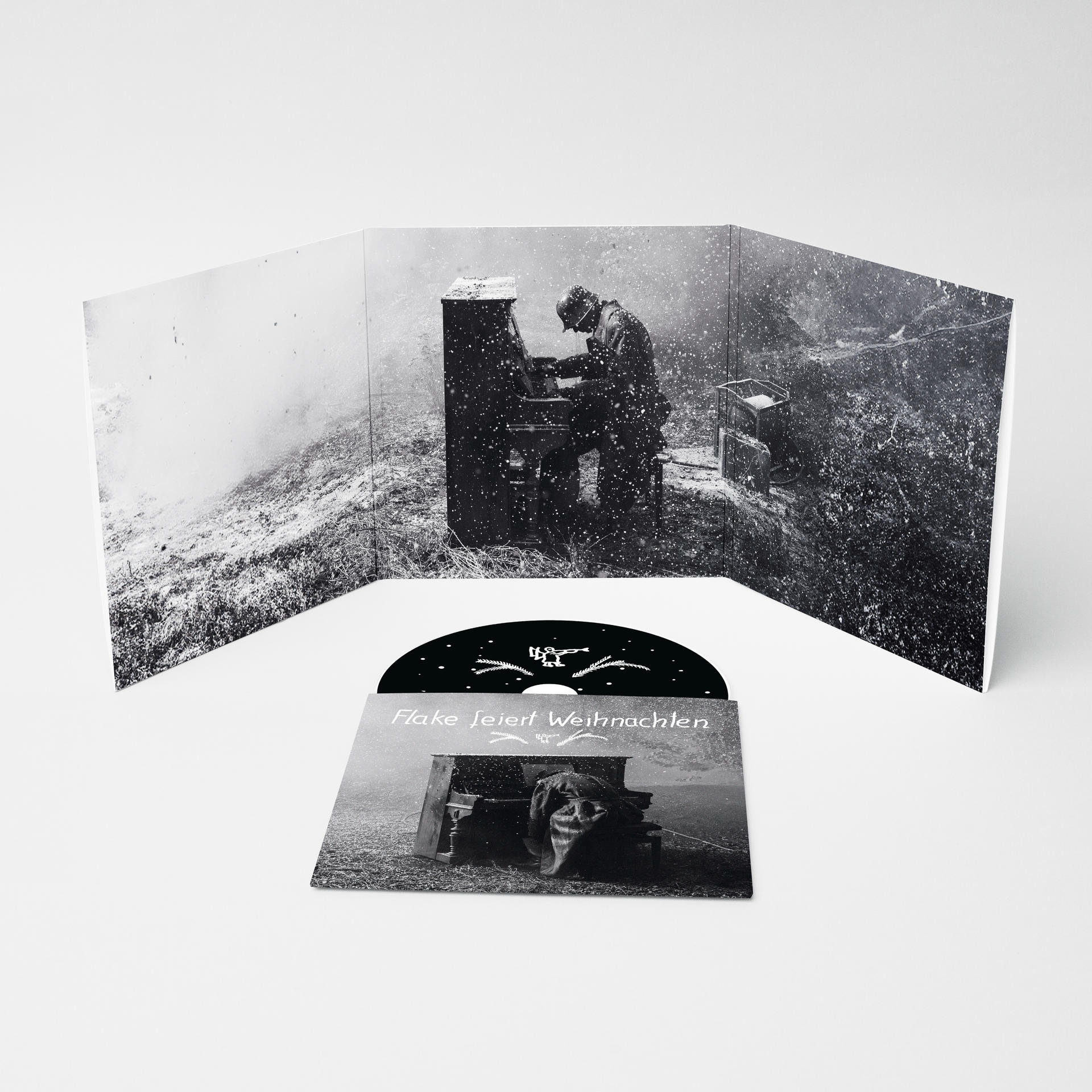 Schwarz-Weiß-Bild einer CD und Albumcover. Eine Person spielt Klavier in einer Schneelandschaft. Text: 'Flake feiert Weihnachten'.