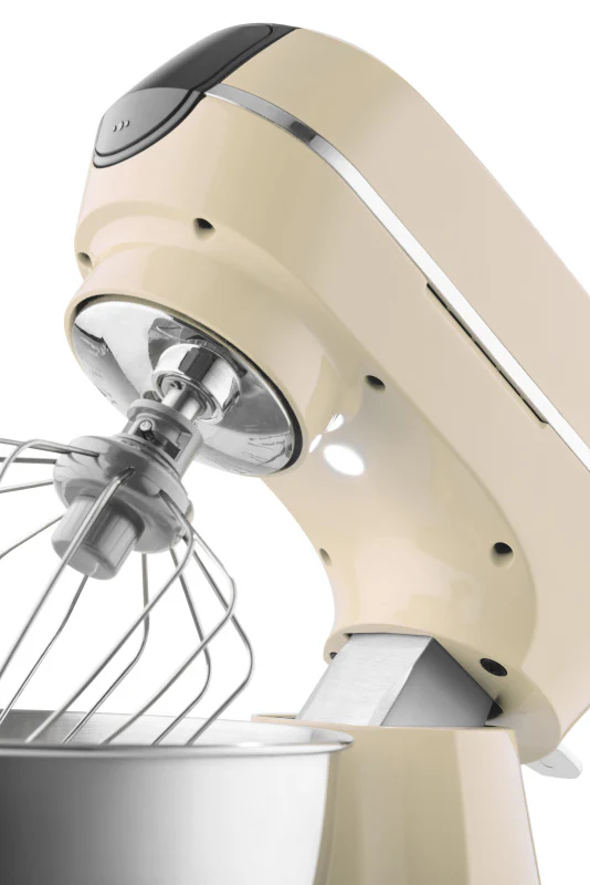 Krémszínű robotgép ezüst keverőtállal és tartozékokkal, fehér háttérrel.