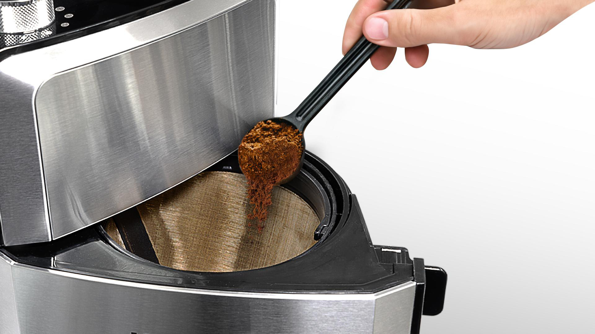 Eine Person, die mit einem schwarzen Löffel Kaffeepulver in eine Kaffeemaschine gibt.