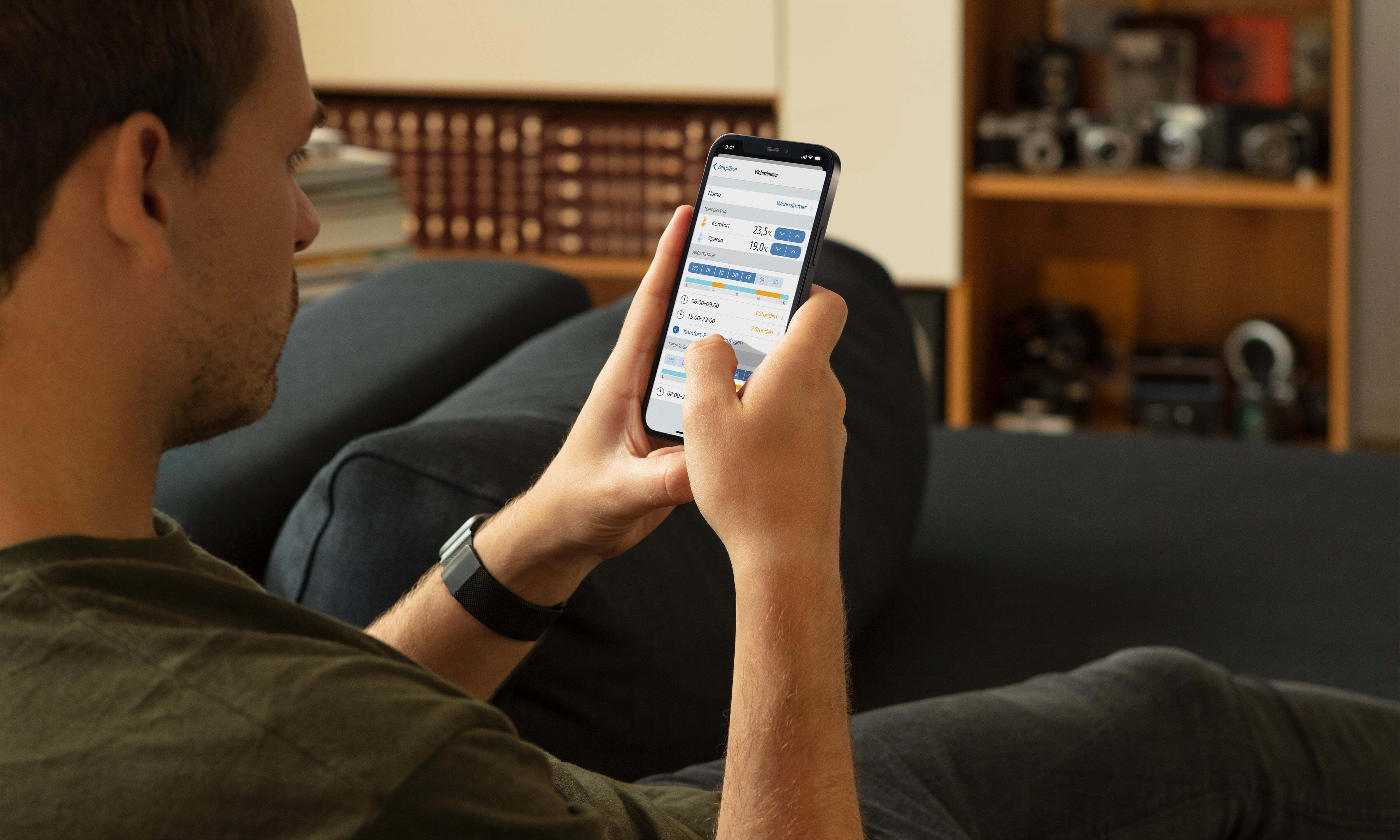 Ein Mann benutzt ein Smartphone, betrachtet einen App-Bildschirm, während er auf einem Sofa sitzt.