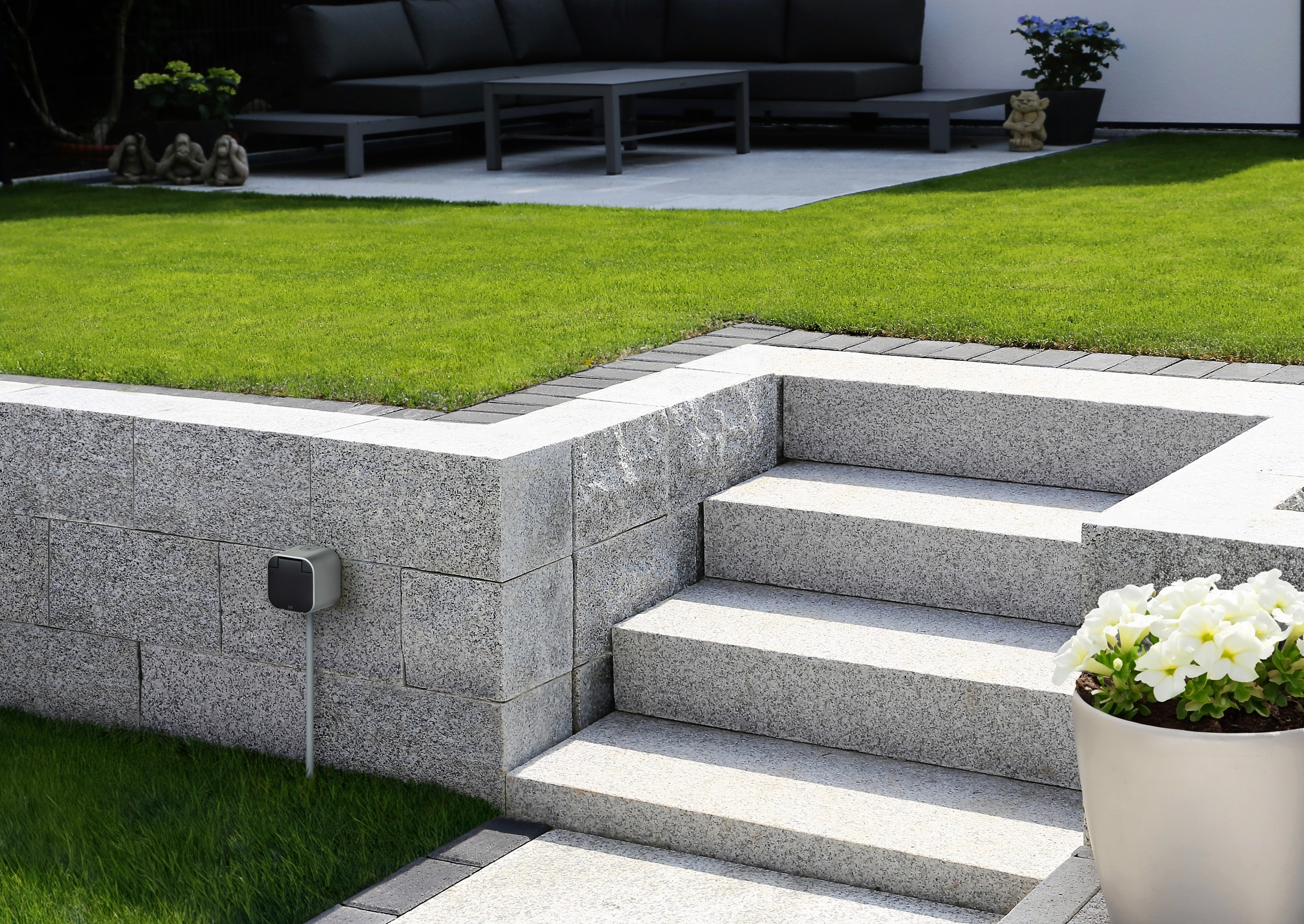 Außenszene mit Treppe, Steinmauer, Gras und einem Lautsprecher.