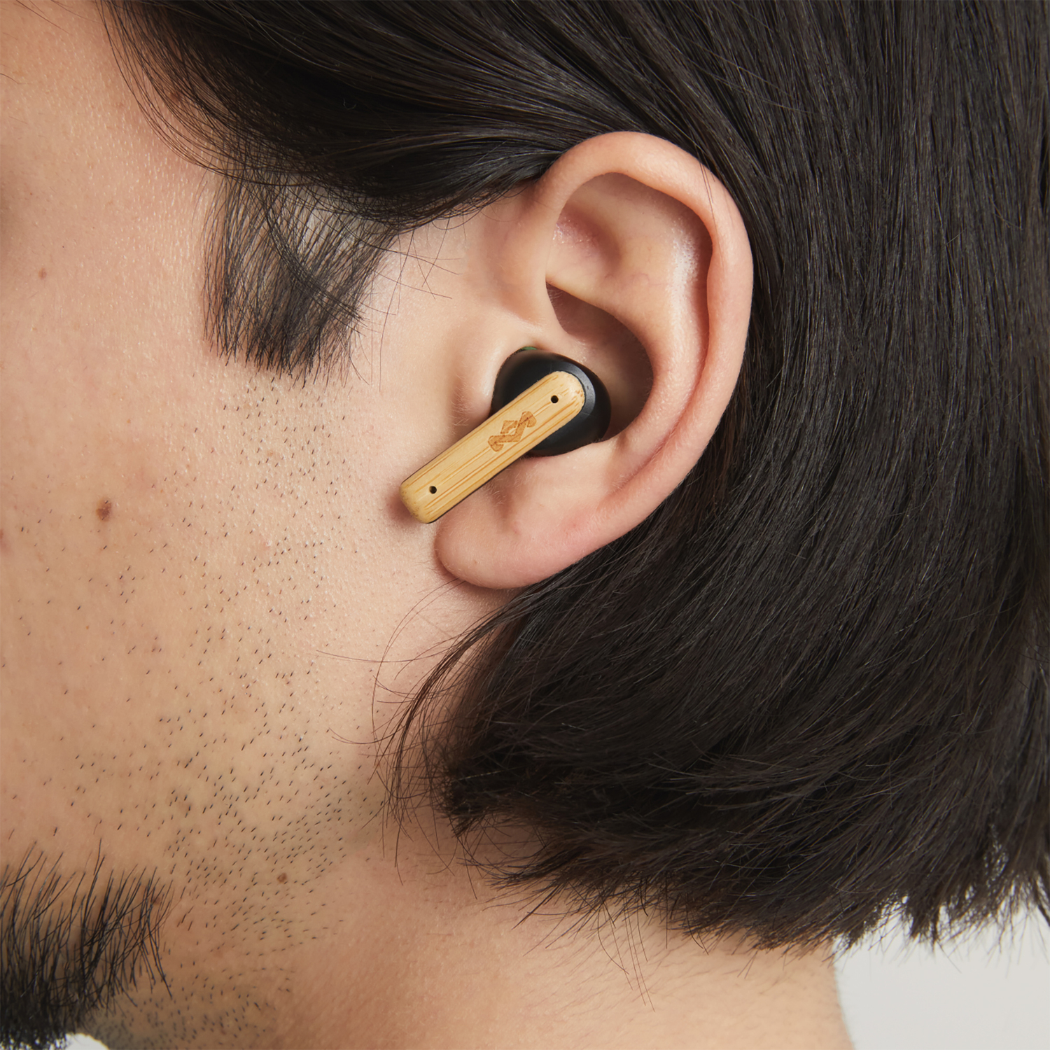 A man wearing a bamboo-looking earbud in his ear.