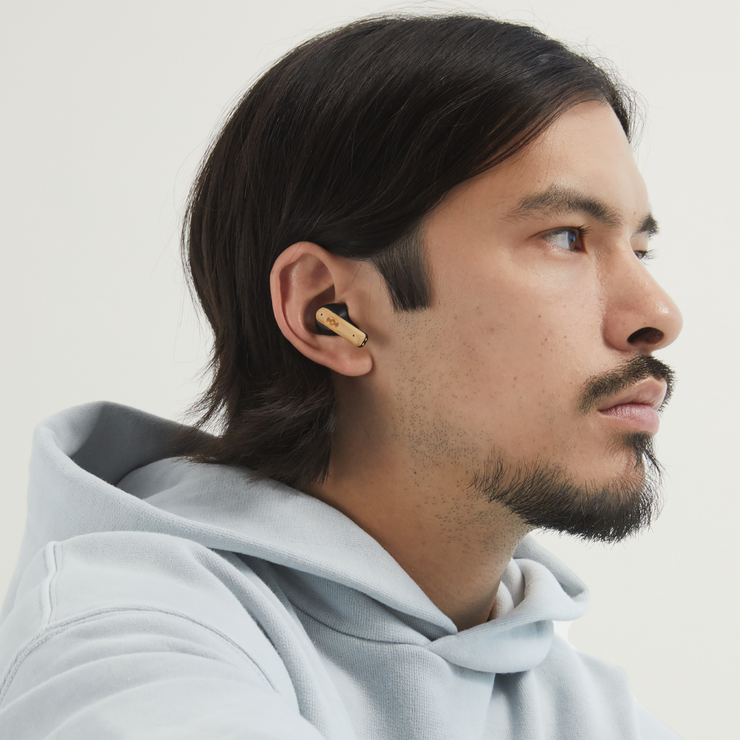 Man wearing earbuds, profile view, wearing a light blue hoodie, white background.