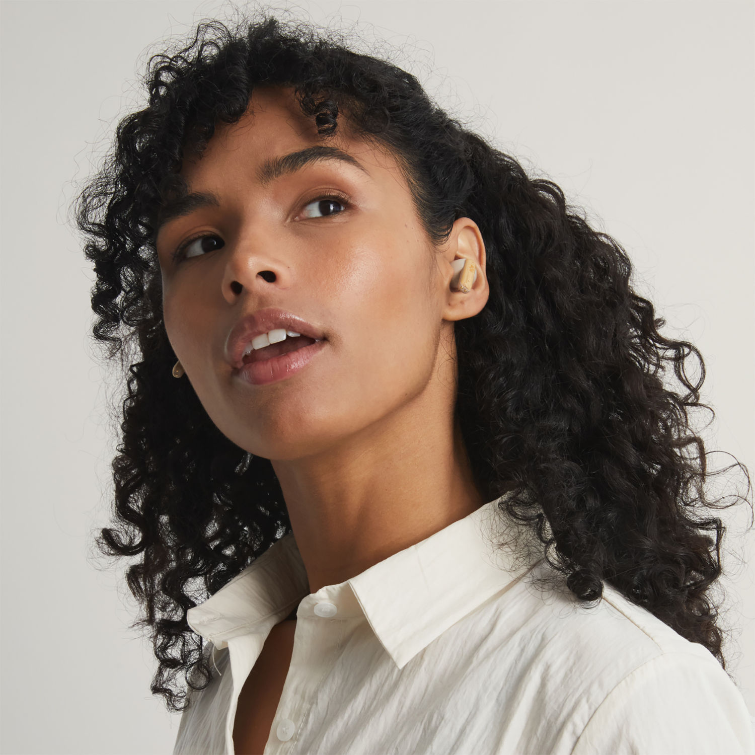 Woman with curly hair, wearing a white shirt and a pair of in-ear headphones.