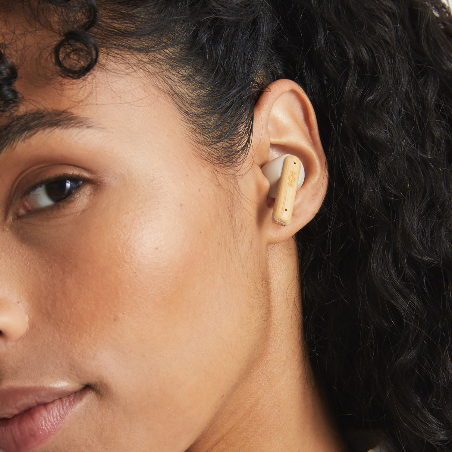 A woman with an earbud in her ear. The earbud is made of bamboo. The background is blurred.