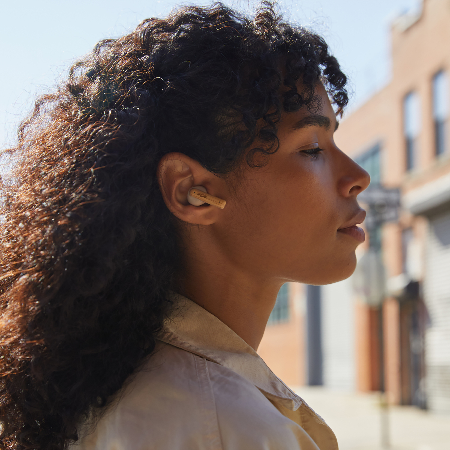 Woman with curly hair wearing an earbud in her ear looking away.