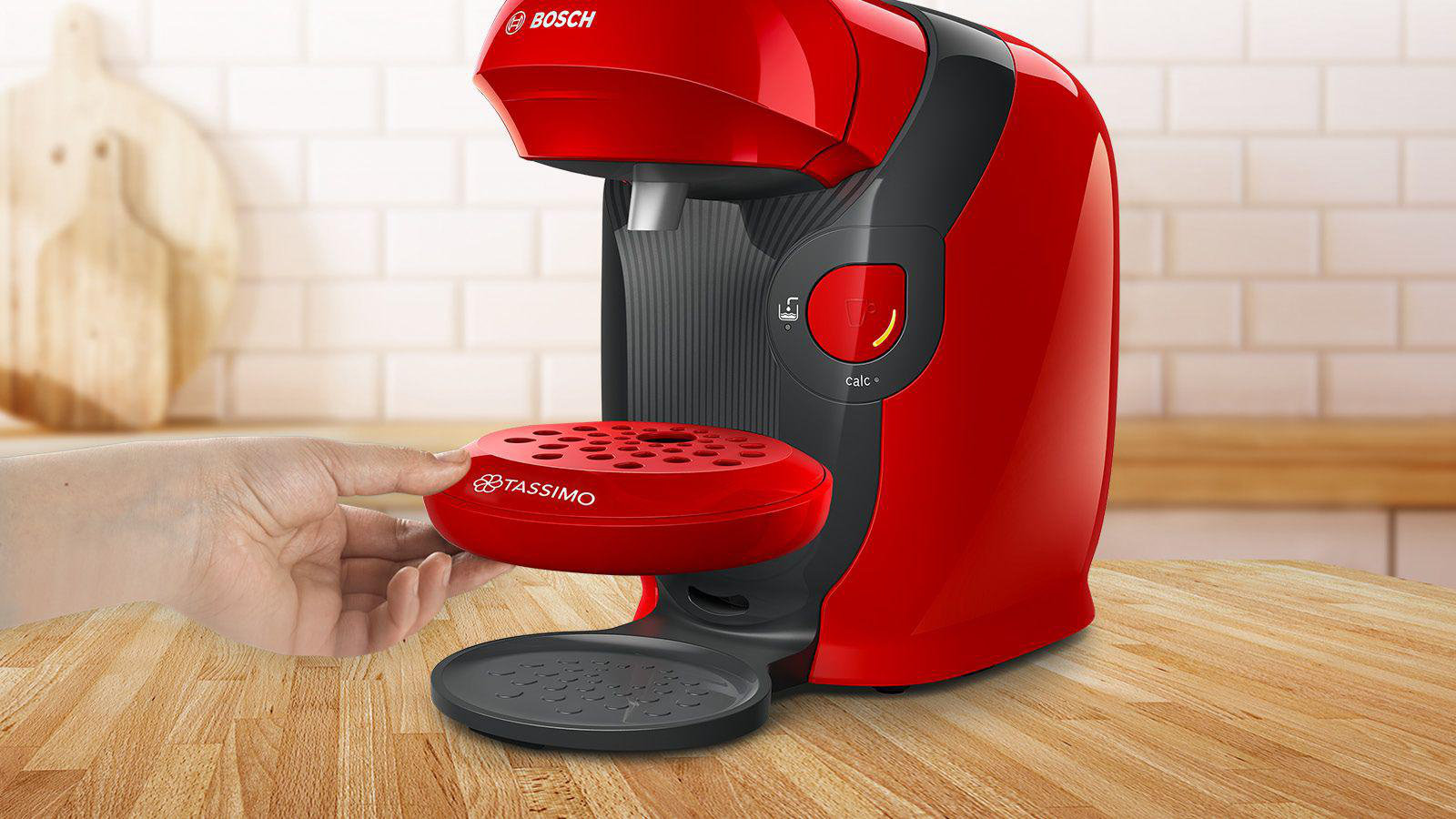 Eine rote Bosch Tassimo Kaffeemaschine, bei der eine Hand dabei ist, das Tablett zu entfernen.