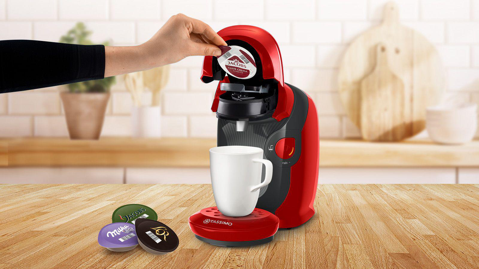Person, die eine Kaffeekapsel in eine rot-schwarze Kaffeemaschine einlegt.