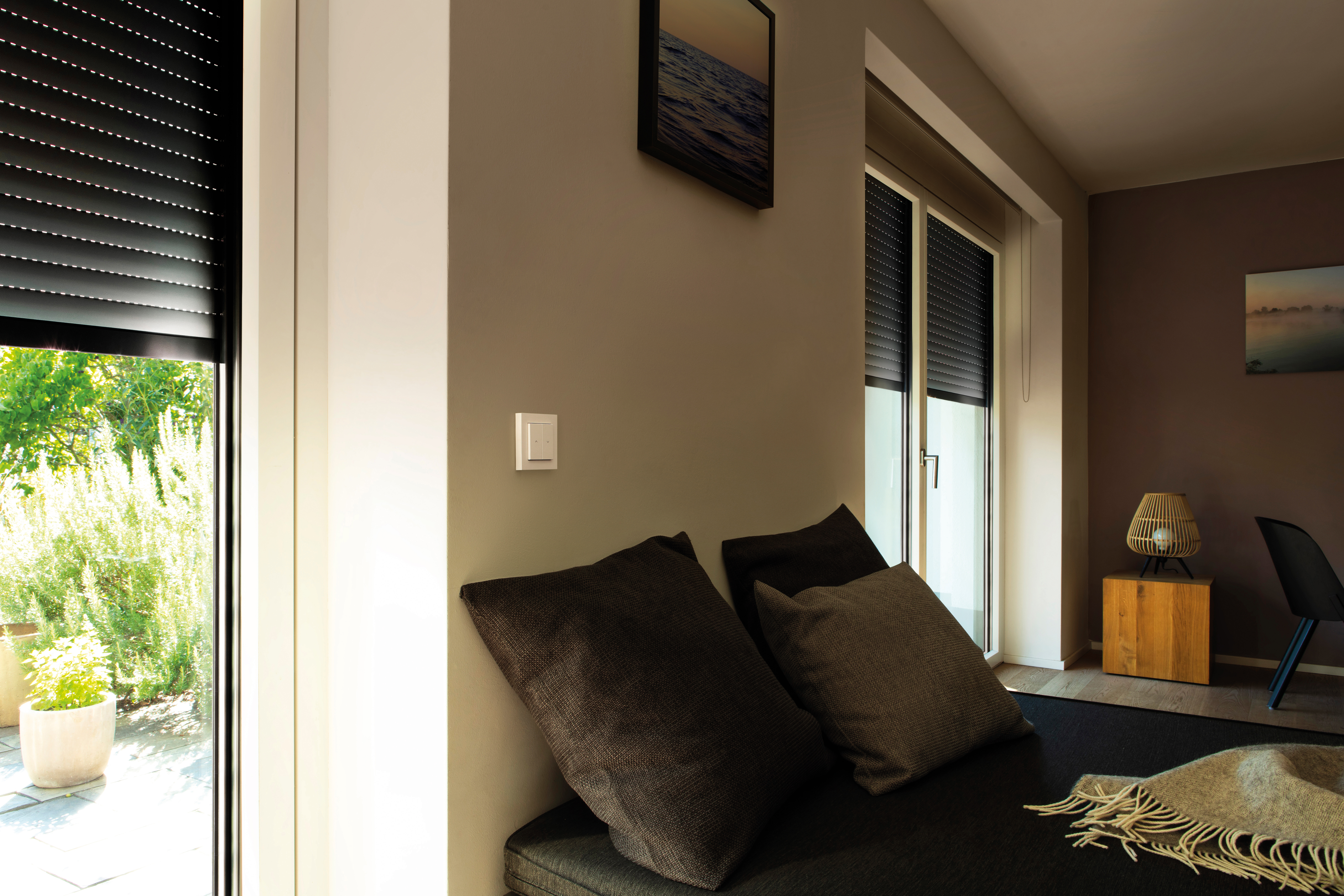 Innenraum mit Fenster, Vorhängen, Lichtschalter und Sofa mit Kissen.