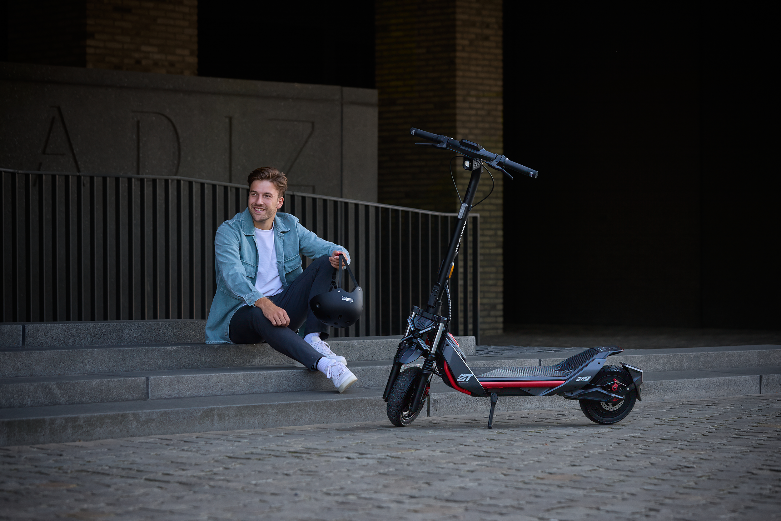 Egy férfi lépcsőn ül egy elektromos roller mellett, mosolyogva.
