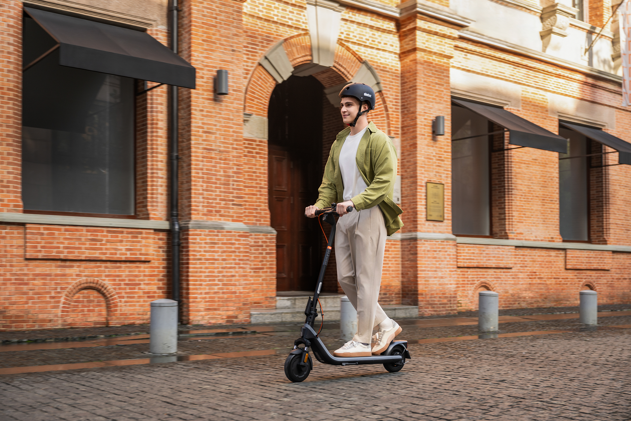 Férfi elektromos robogóval közlekedik a téglás utcán.
