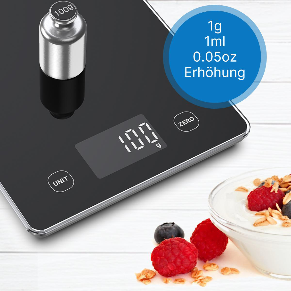 Eine schwarze Digitalwaage zeigt 100g. Daneben eine Schüssel Joghurt mit Himbeeren und Blaubeeren.