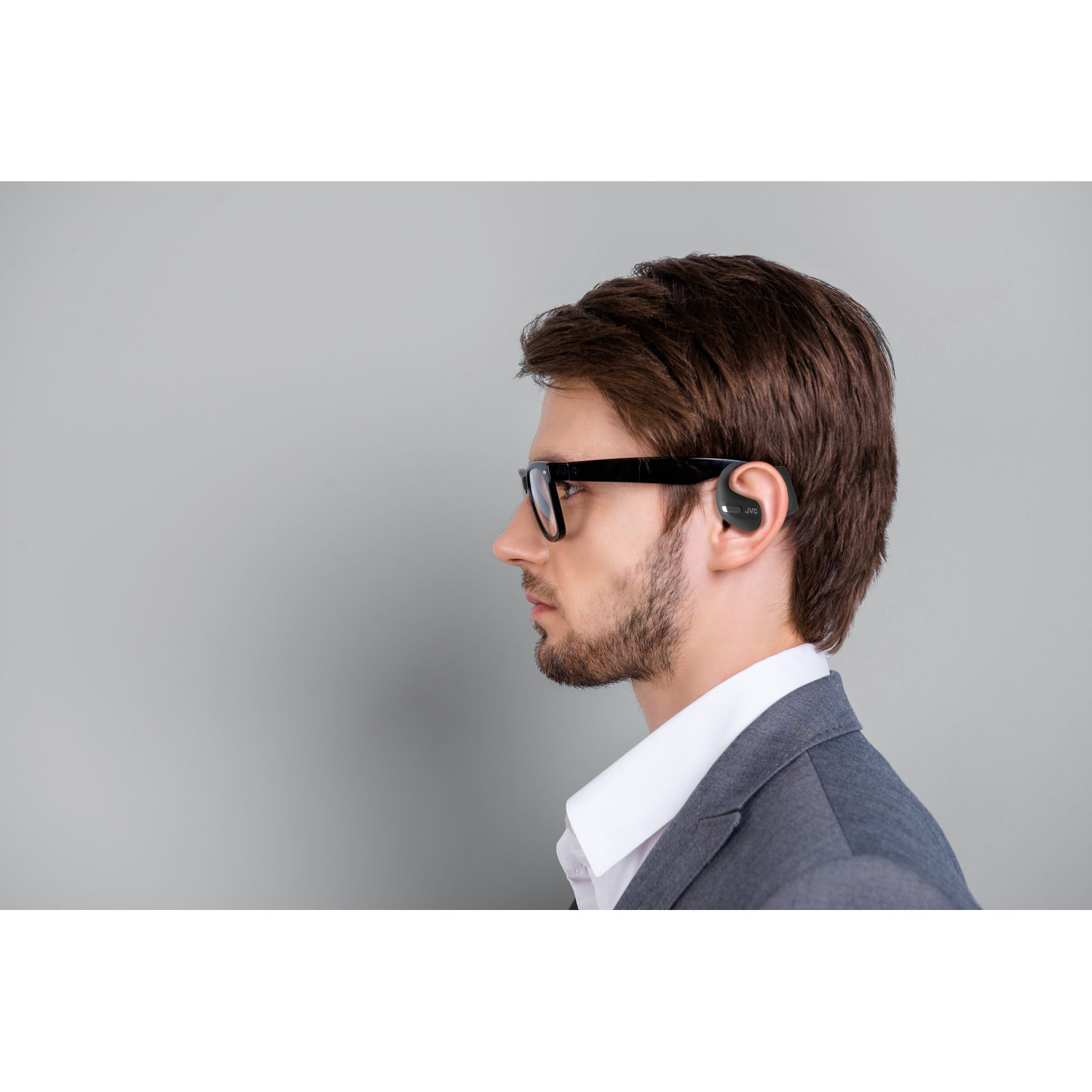 Un homme en lunettes et en costume a un écouteur dans l'oreille, regardant ailleurs.