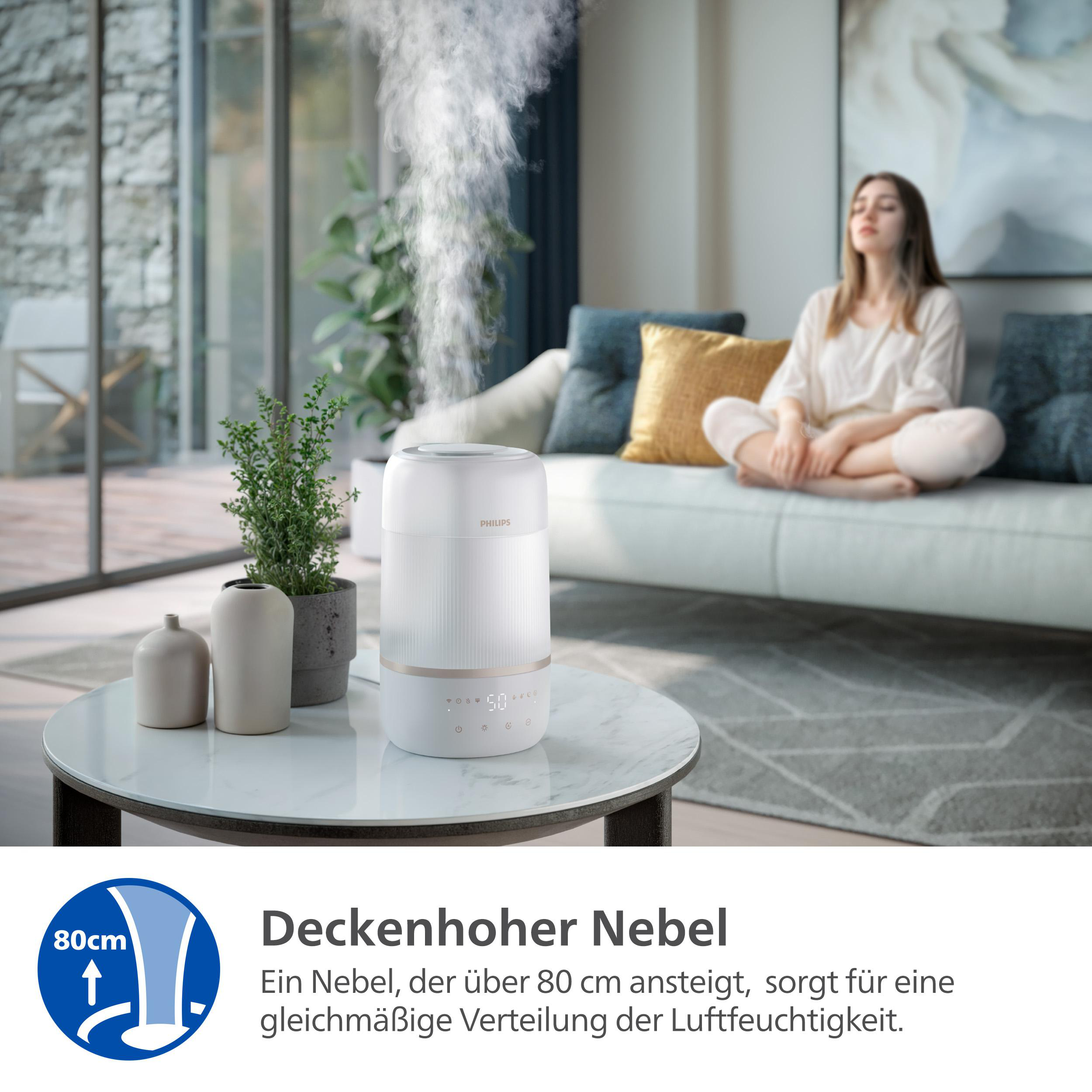 Ein Philips-Luftbefeuchter gibt Dampf ab. Eine Frau sitzt auf einem Sofa. Text sagt 'Deckenhoher Nebel' und '80cm'.